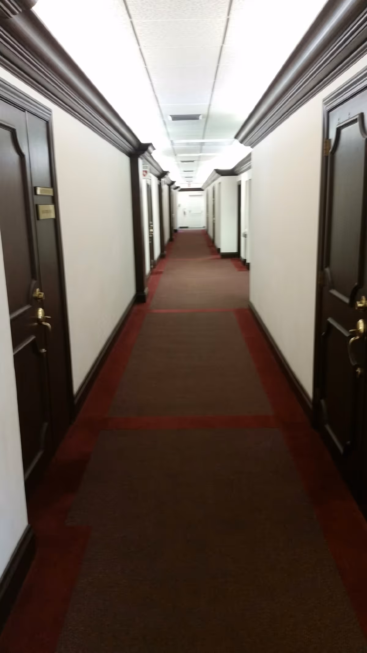 Wide carpeted hallway in a senior living facility with doors along both sides.