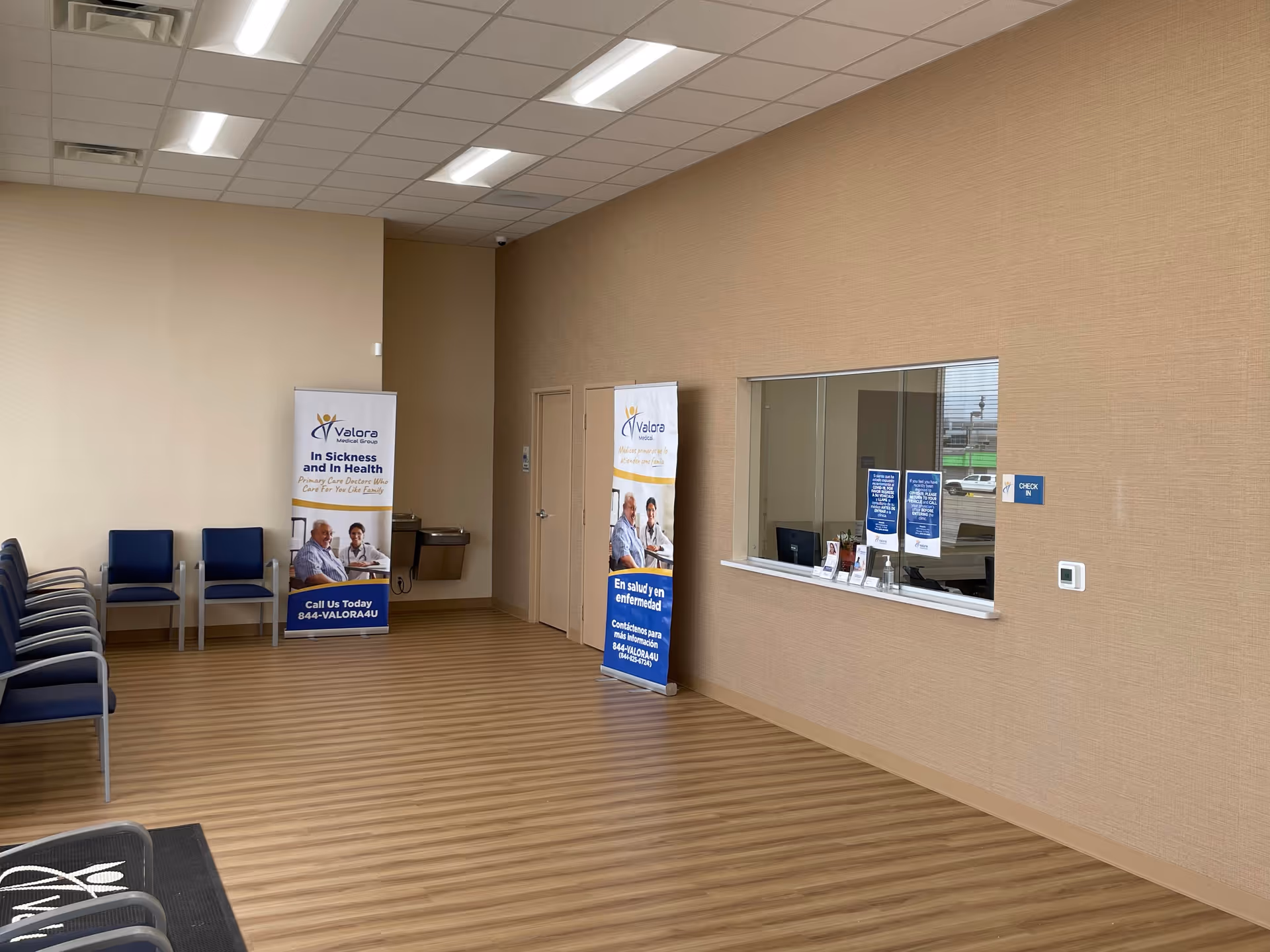 Waiting area with blue chairs, banners, and a reception window along beige walls and wood floor.