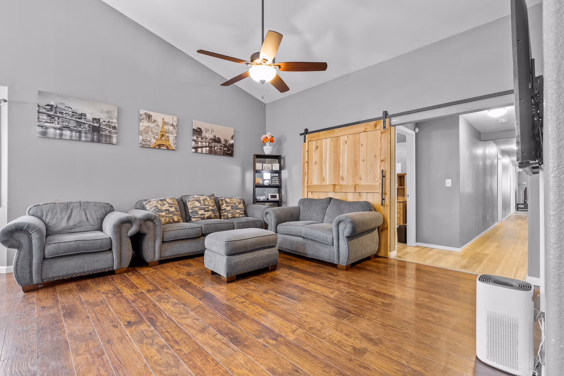 Gray living room with sofas, wood floors, ceiling fan, and a sliding barn door.