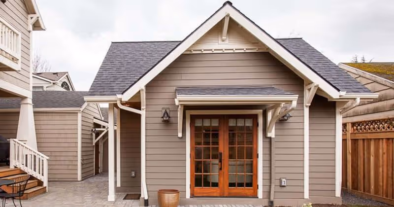 Front view of a gray-sided building with wooden double doors and a small covered entrance.