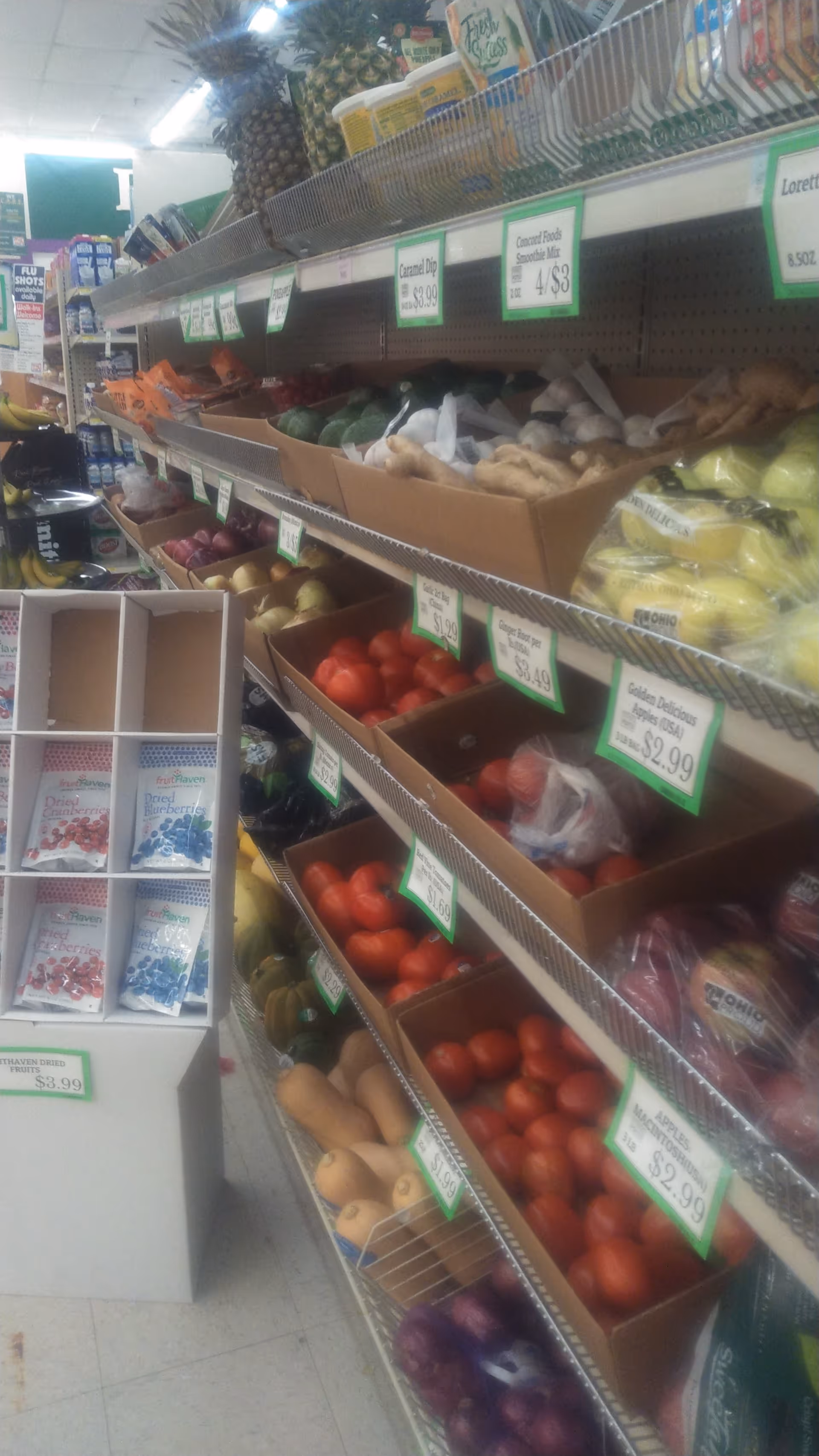 Inside Discount Drug Mart, a grocery aisle shows fruit, vegetables, and price tags on metal shelves.