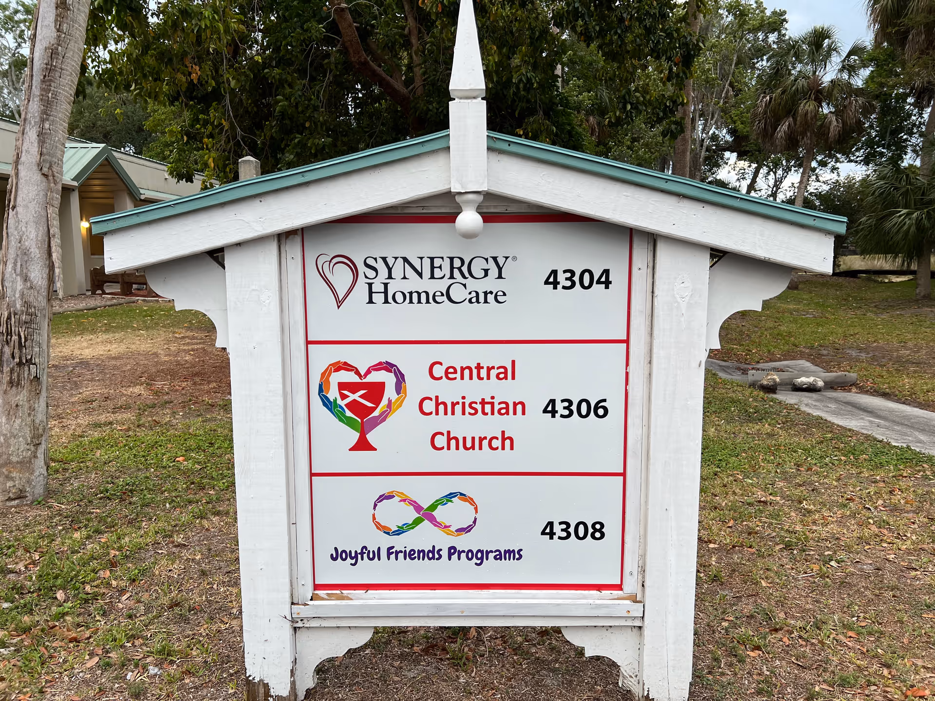 Outdoor wooden signboard showing Synergy HomeCare and Central Christian Church names.