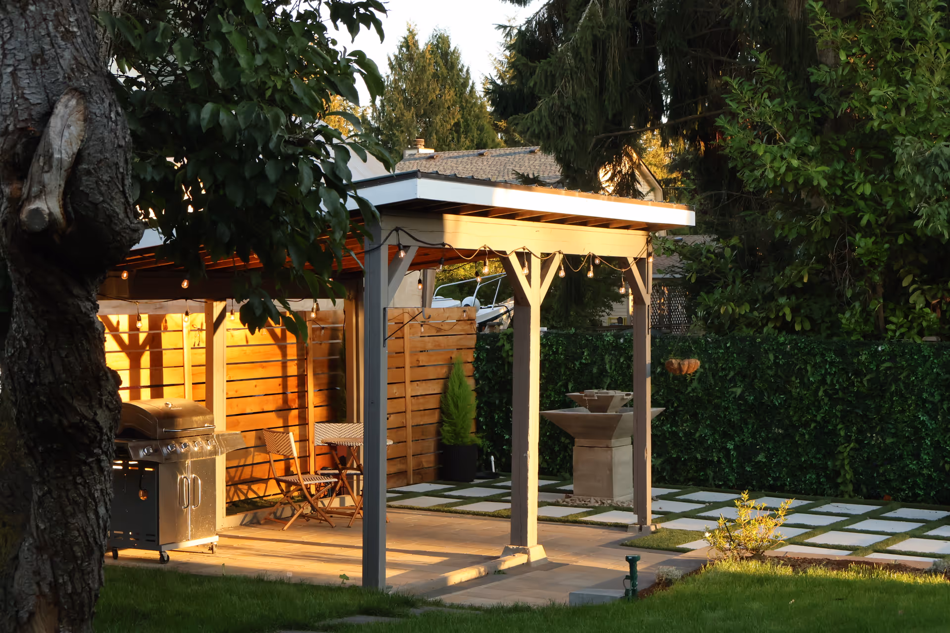 An outdoor patio with a pergola, string lights, grill, seating, and stone path.