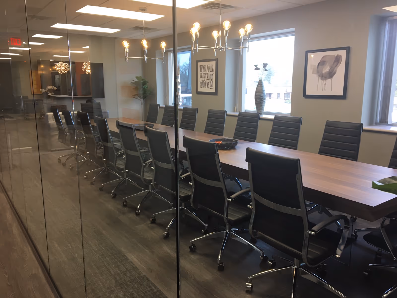 Glass-walled conference room with a long wooden table and black swivel chairs