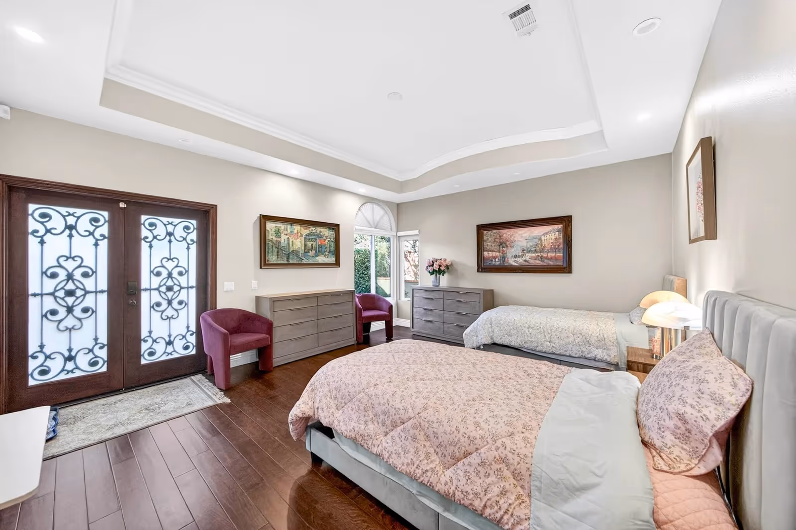 Two beds with pink quilts in a spacious bedroom with dressers and chairs.
