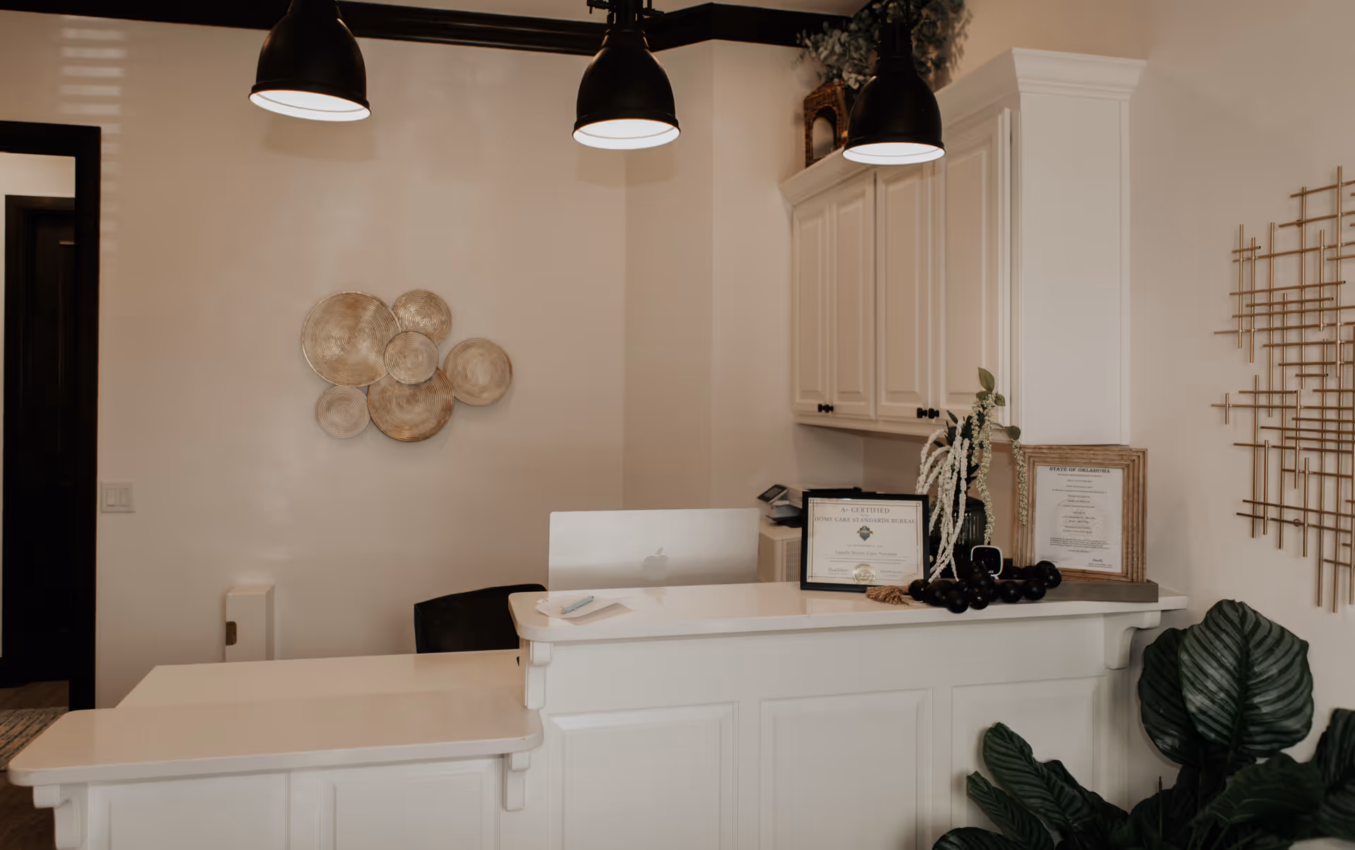 Reception desk in a bright, modern lobby with certificates, plants, and decorative art.