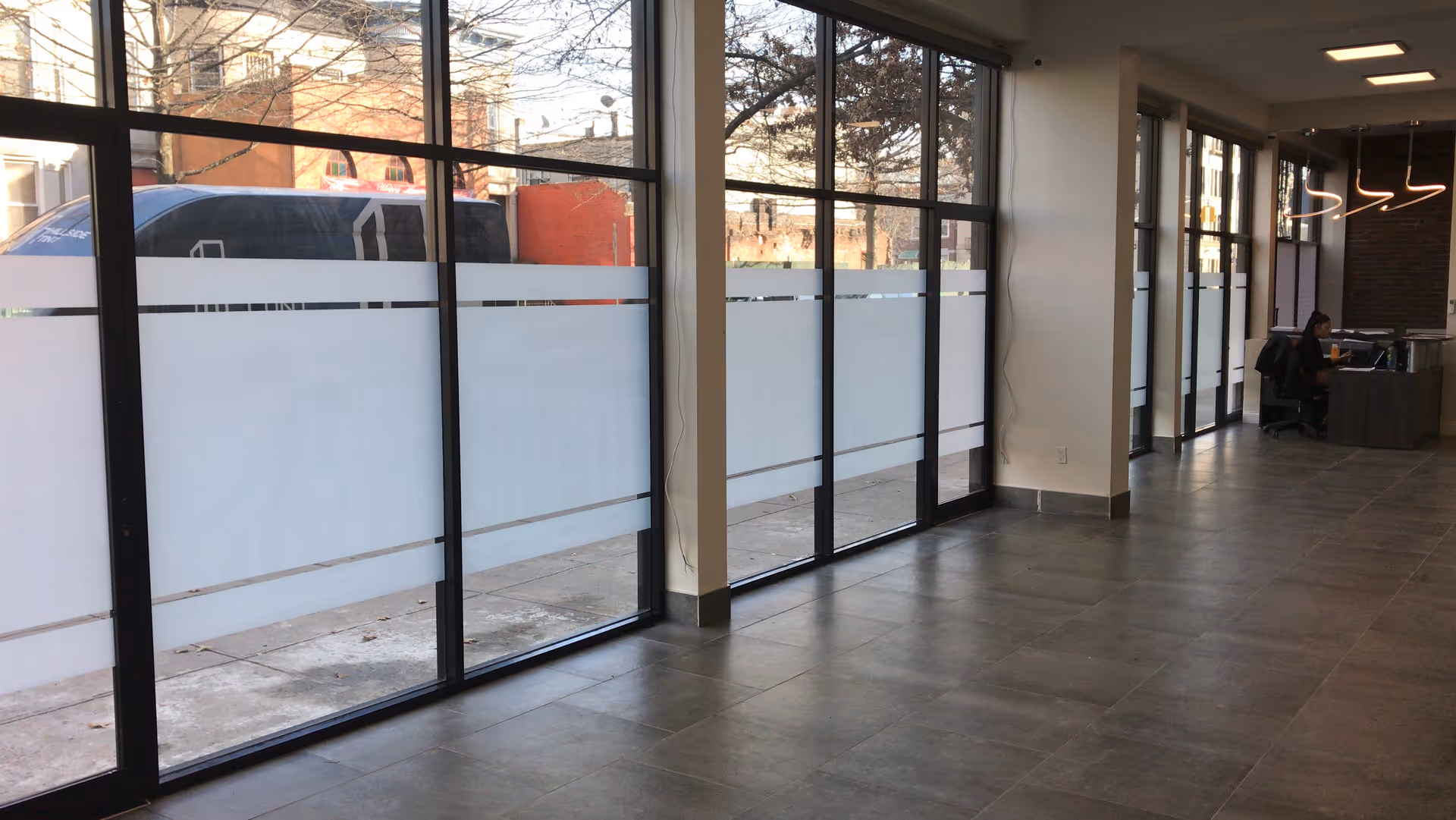 Bright hallway lobby with large windows and frosted panels; a receptionist works at a desk.