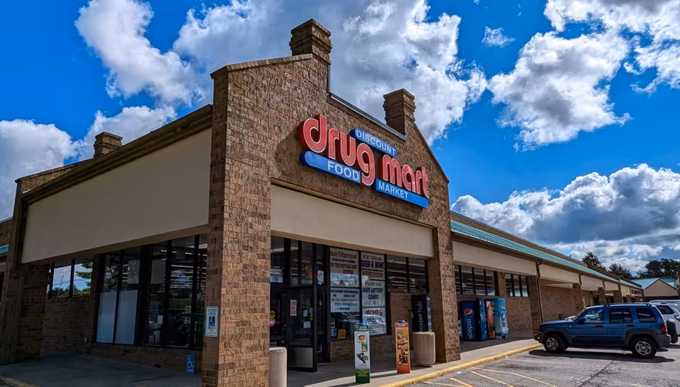 Exterior view of Discount Drug Mart storefront with brick facade, signage, and parked cars.