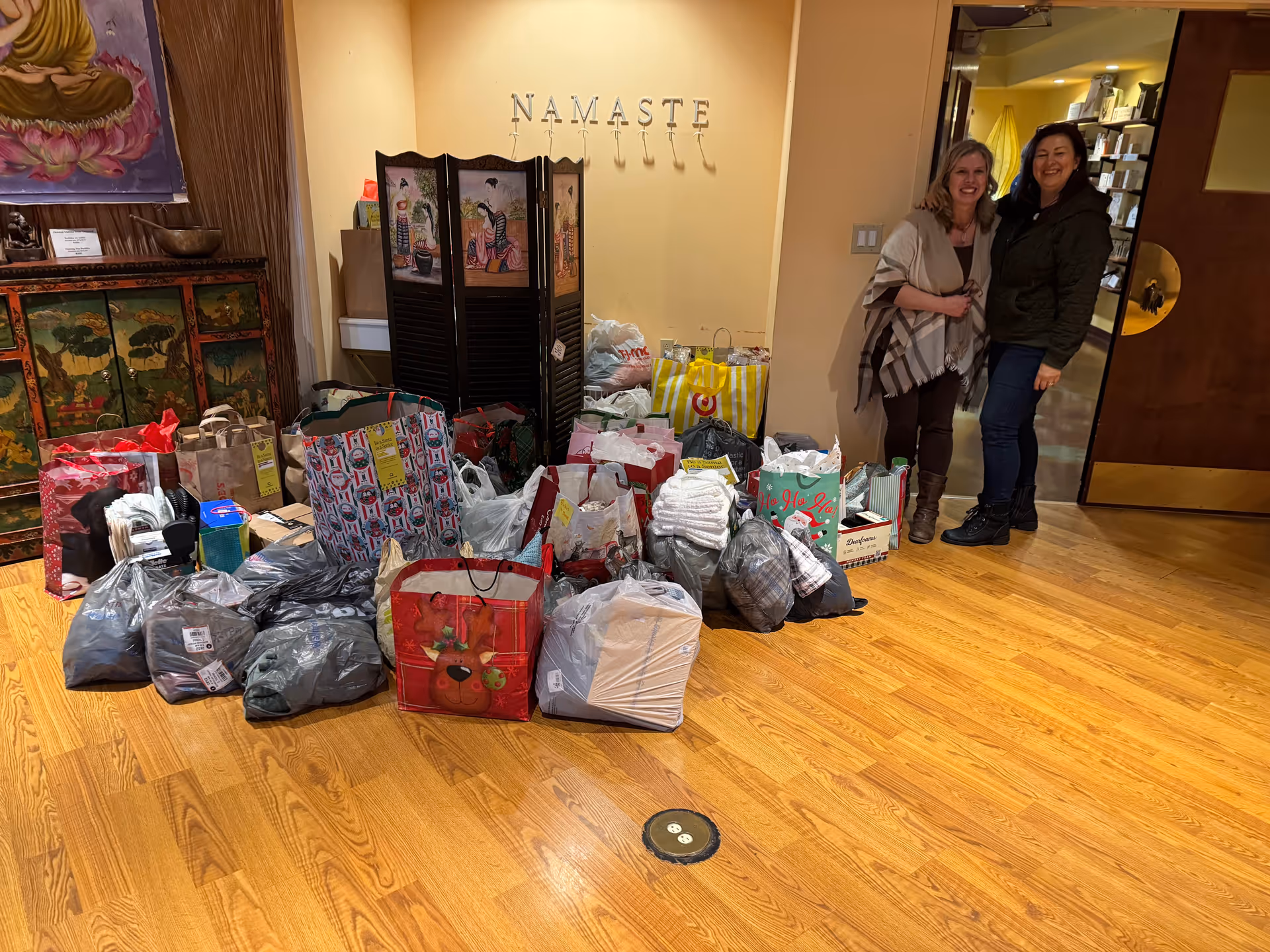 Two women stand beside a large pile of gift bags and boxes in a lobby.