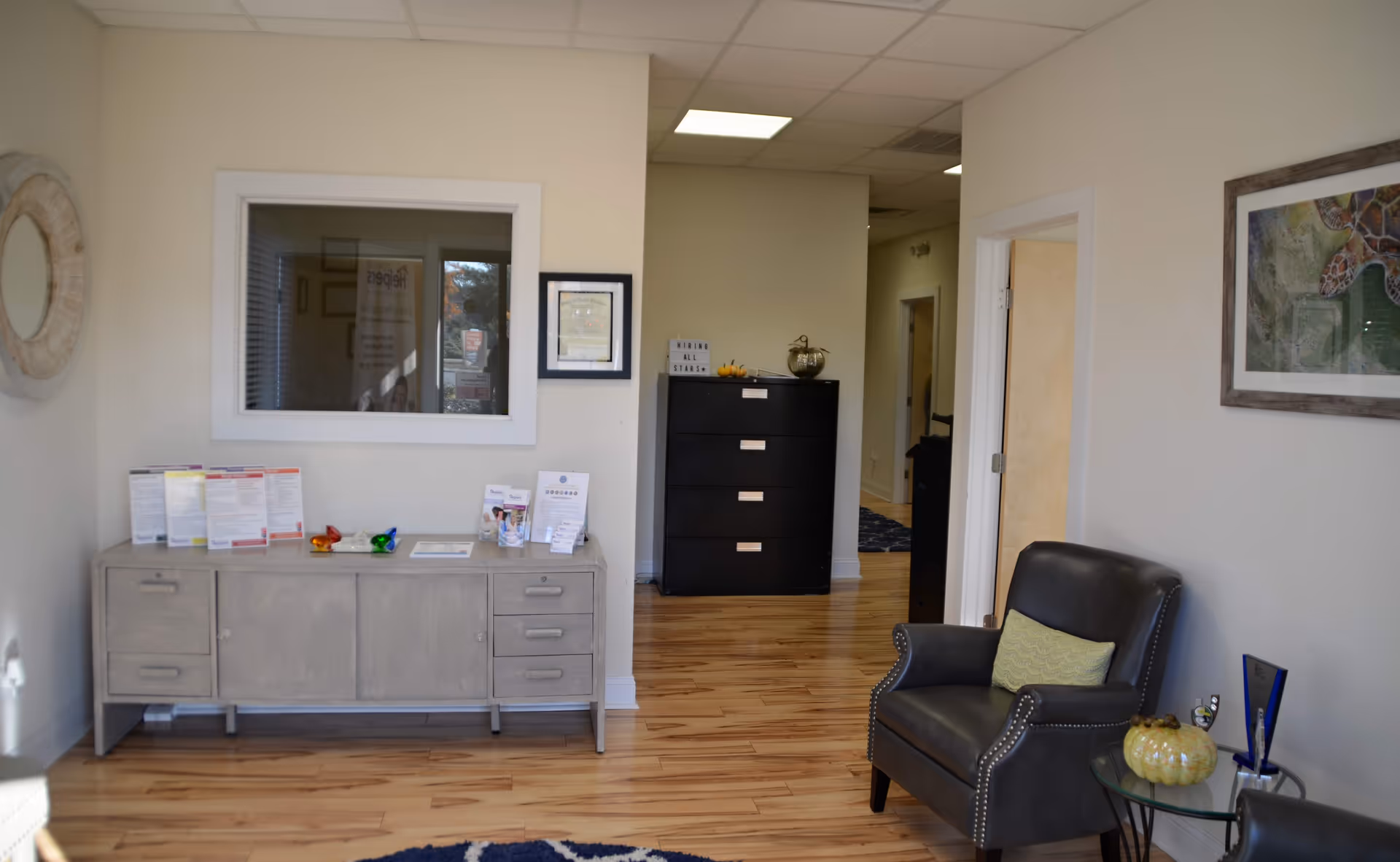 Interior reception area with gray console, black chair, doorway, and artwork in a senior living facility.