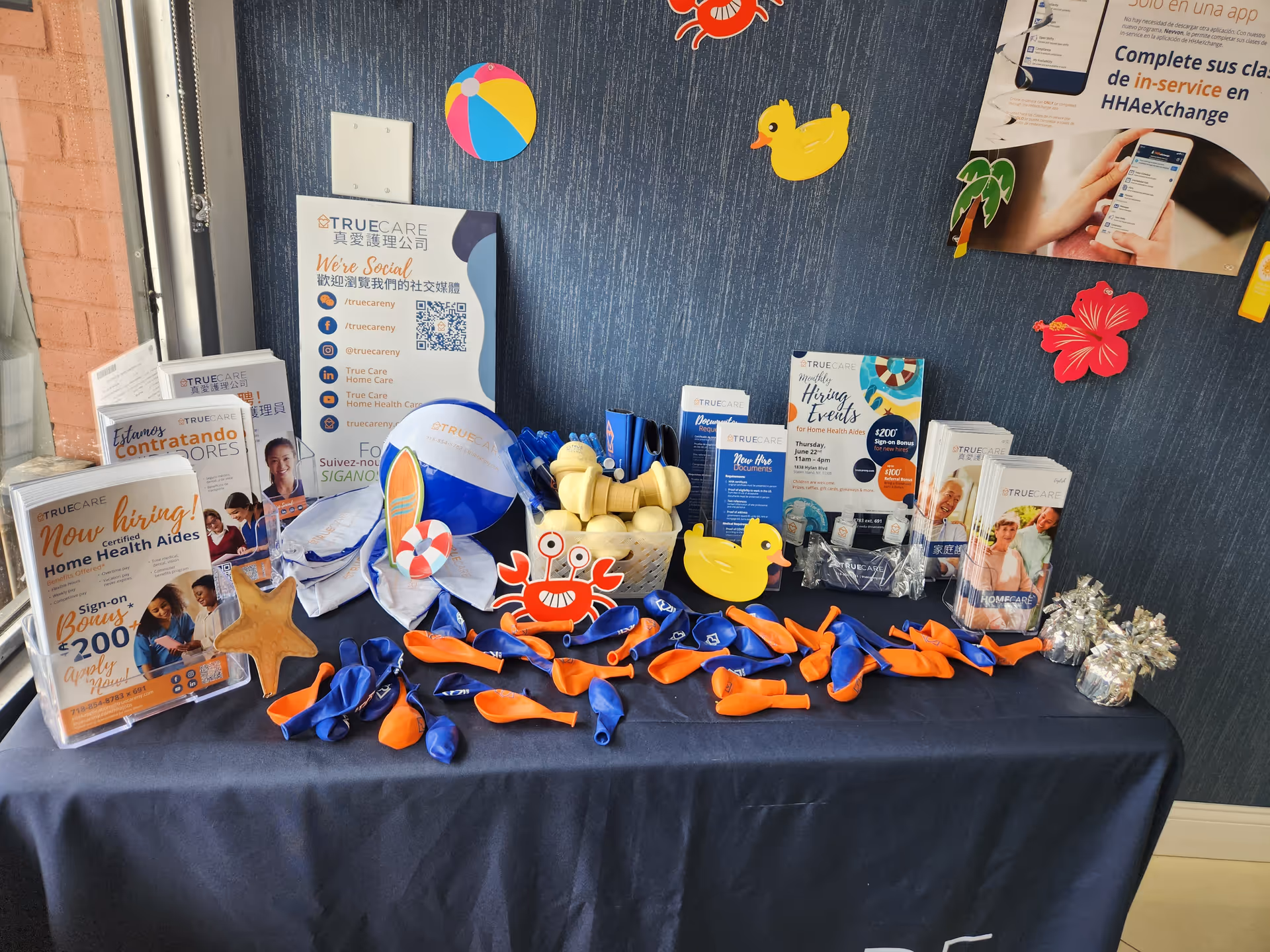 A display table with TrueCare promotional brochures, balloons, and orange-blue ribbons on a dark tablecloth.