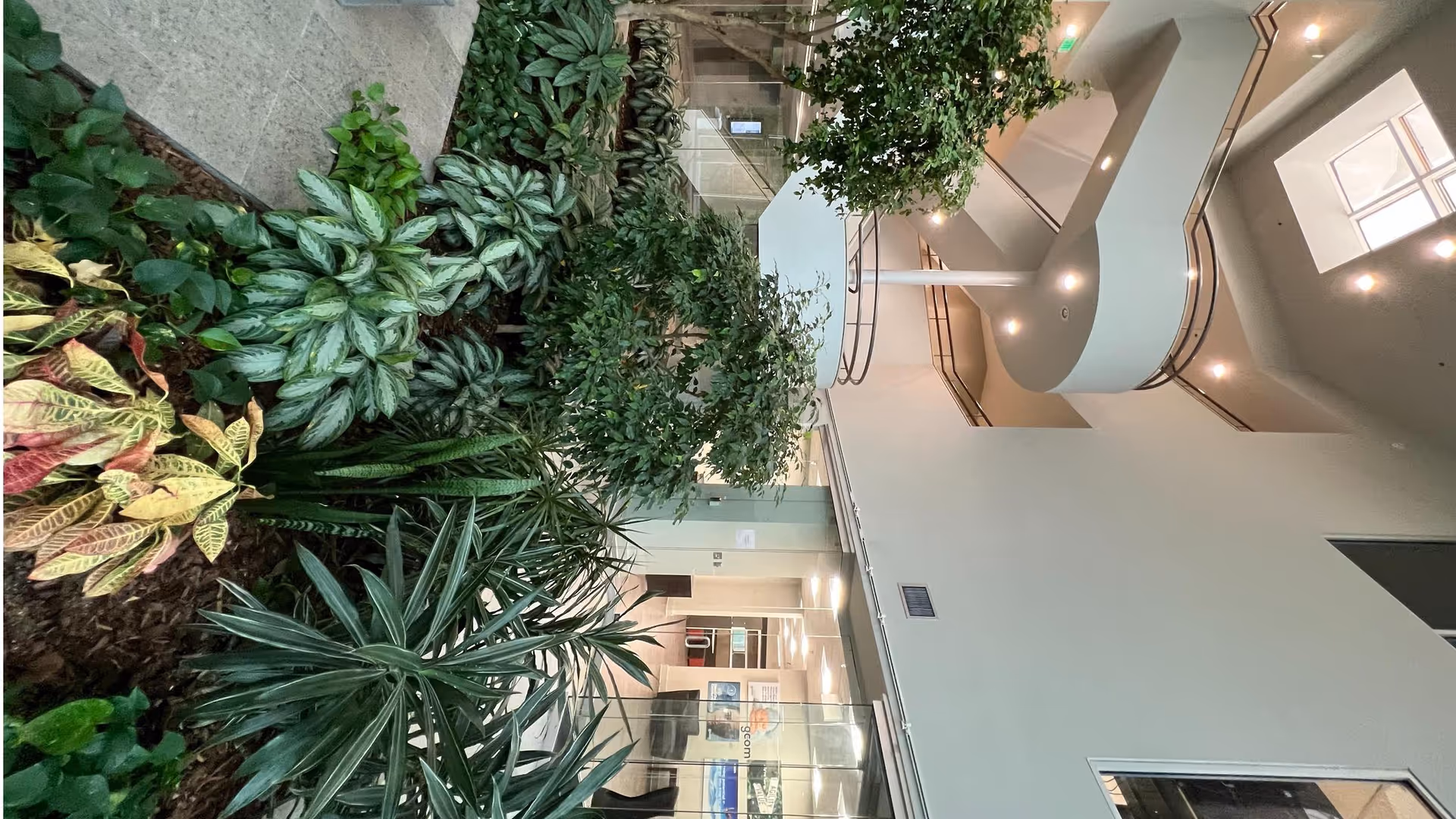 Indoor atrium with lush greenery, glass railings, and curved staircases.
