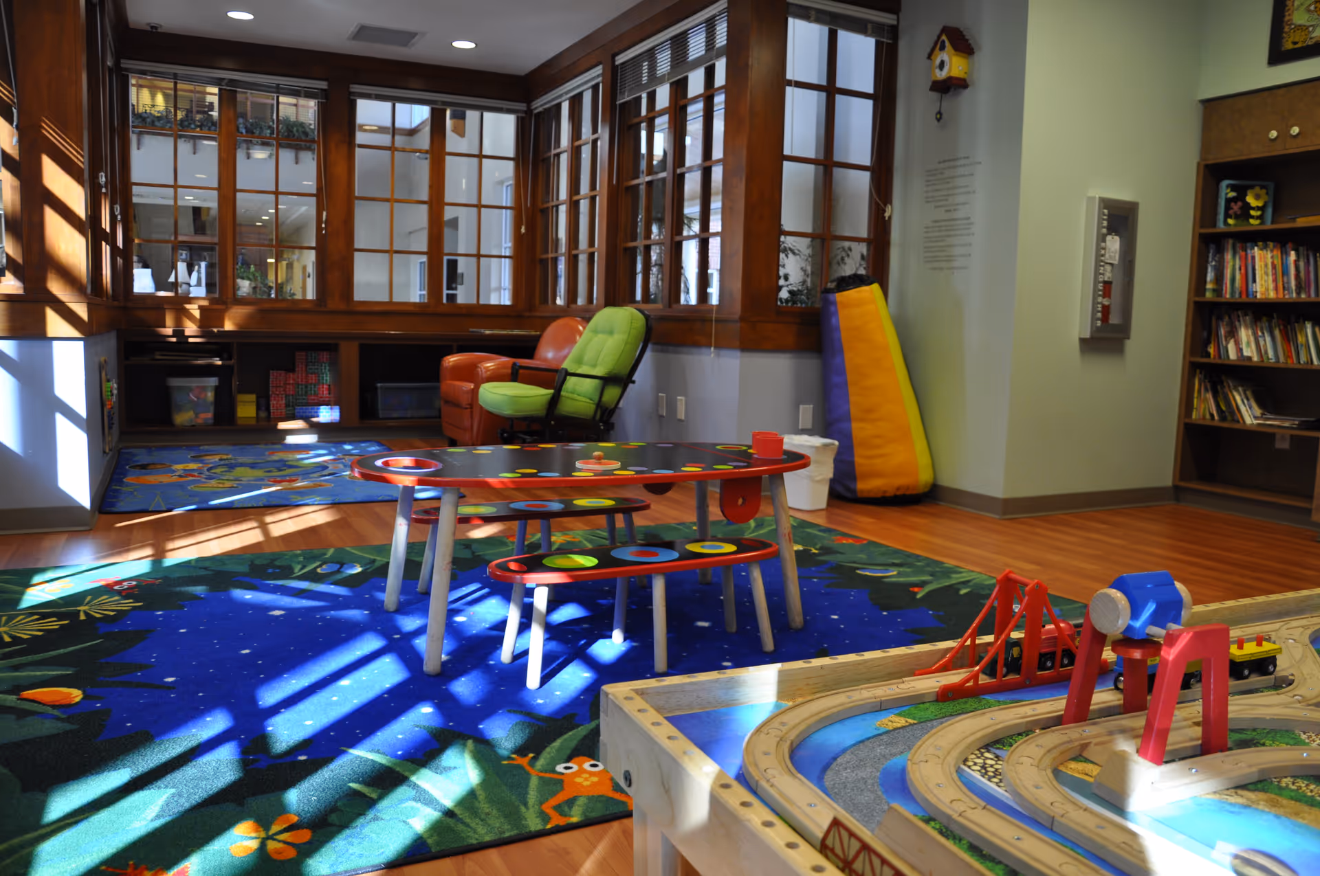 Colorful indoor play area with a toy train set, tables, and a bookshelf.