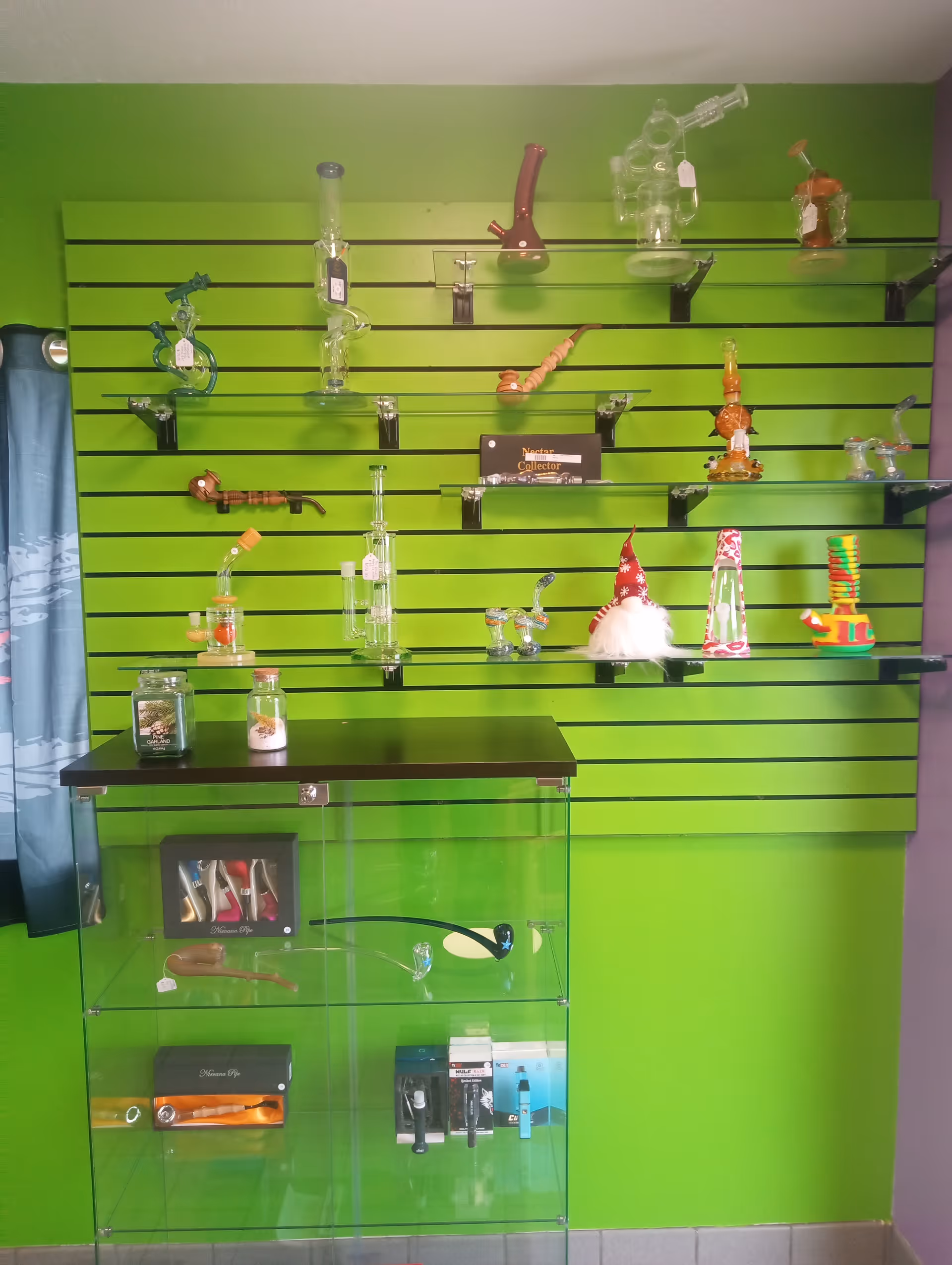 Bright green wall with slatted shelves displaying glass pipes and novelty items.