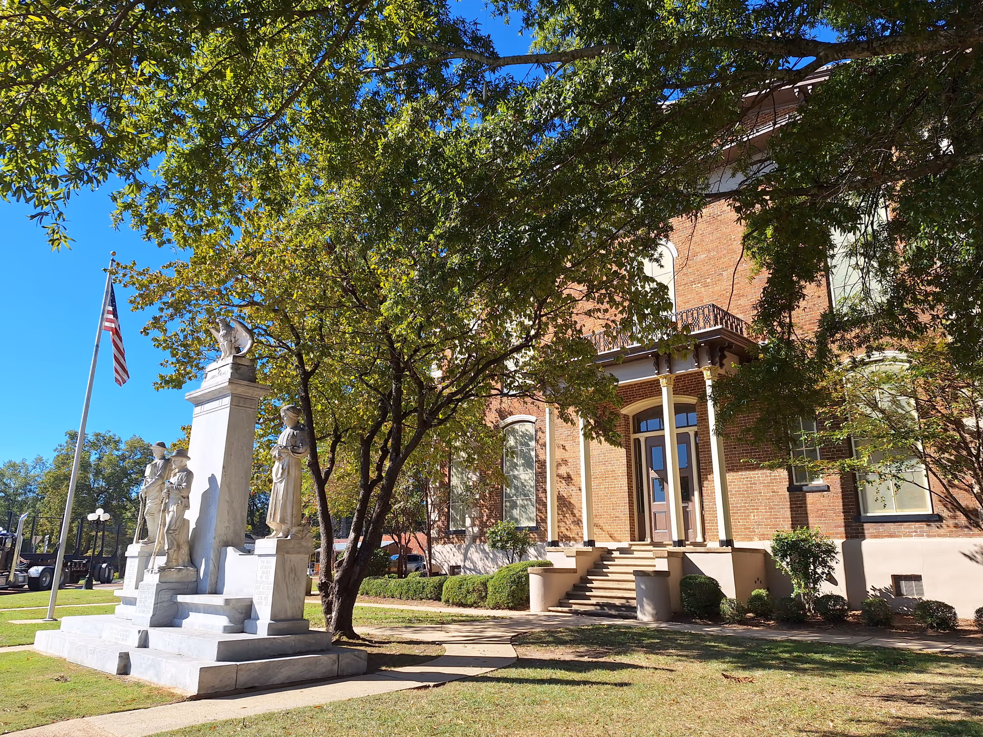 Brick building front with steps, columns, statues, and a waving American flag.