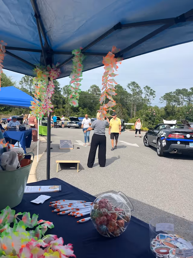 Outdoor senior living event with tents, tables, leis, and attendees in a parking lot.