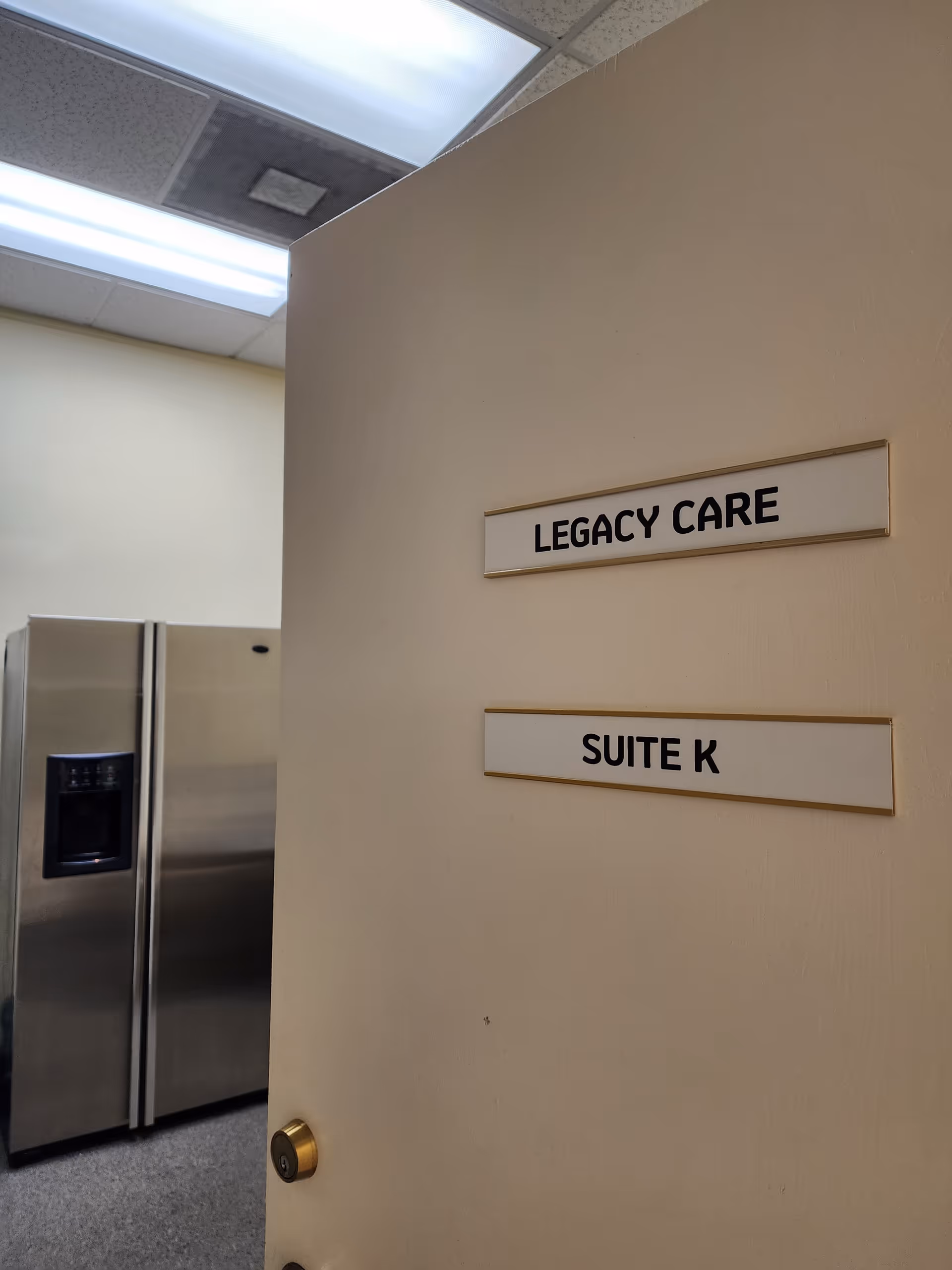 Beige hallway wall with Legacy Care and Suite K signs, refrigerator visible.
