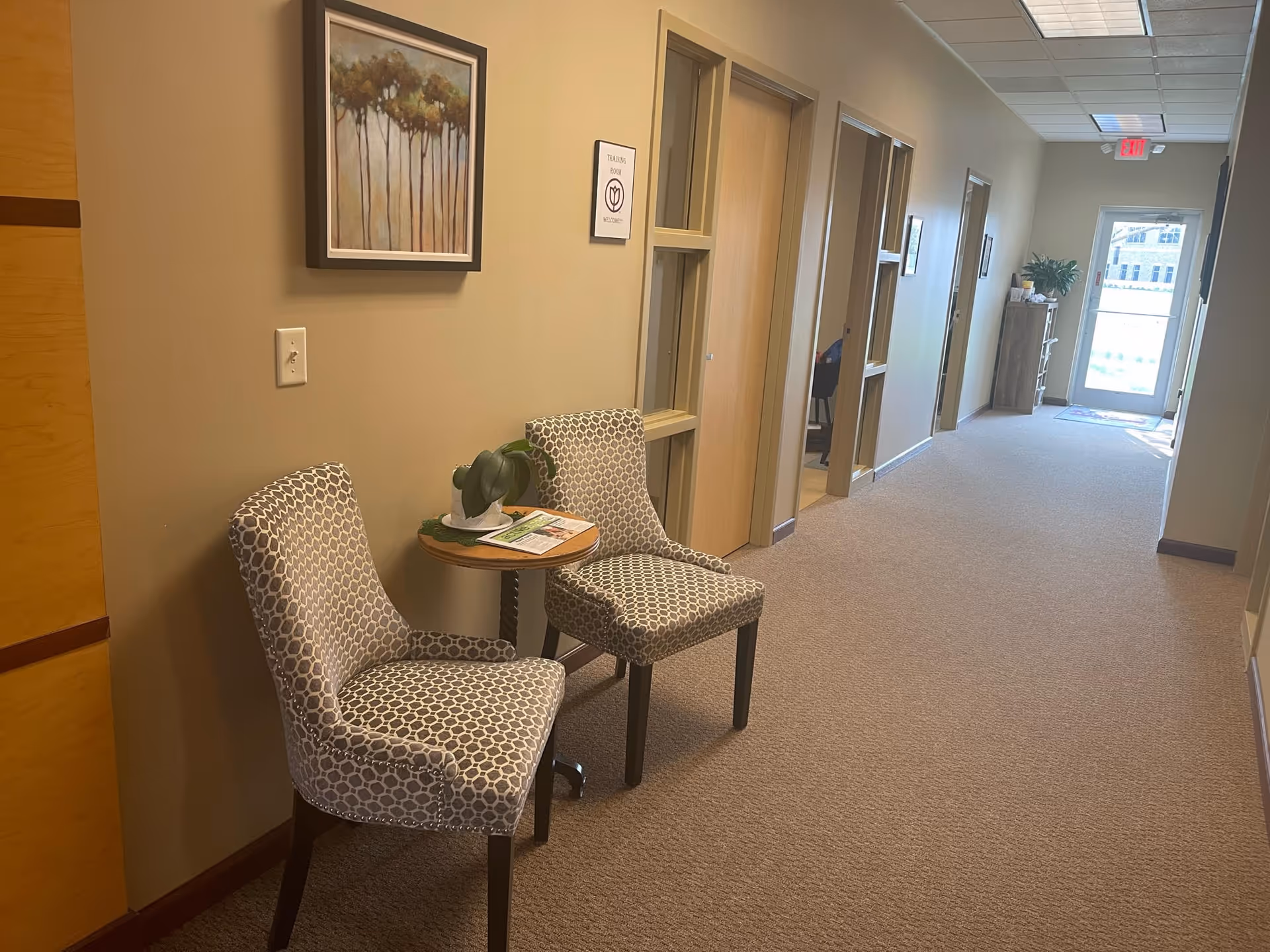 A hallway in a senior living facility with two patterned chairs and a small table.