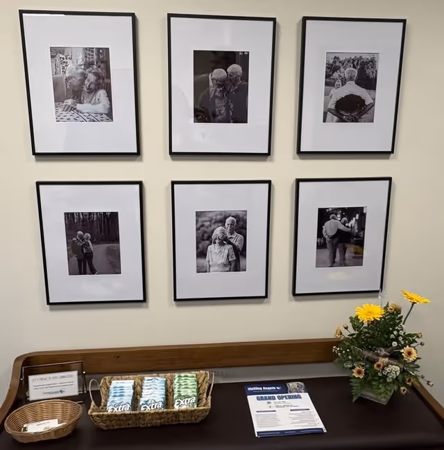 Interior wall with six framed black and white photos, a bench, flowers, and a snack counter.