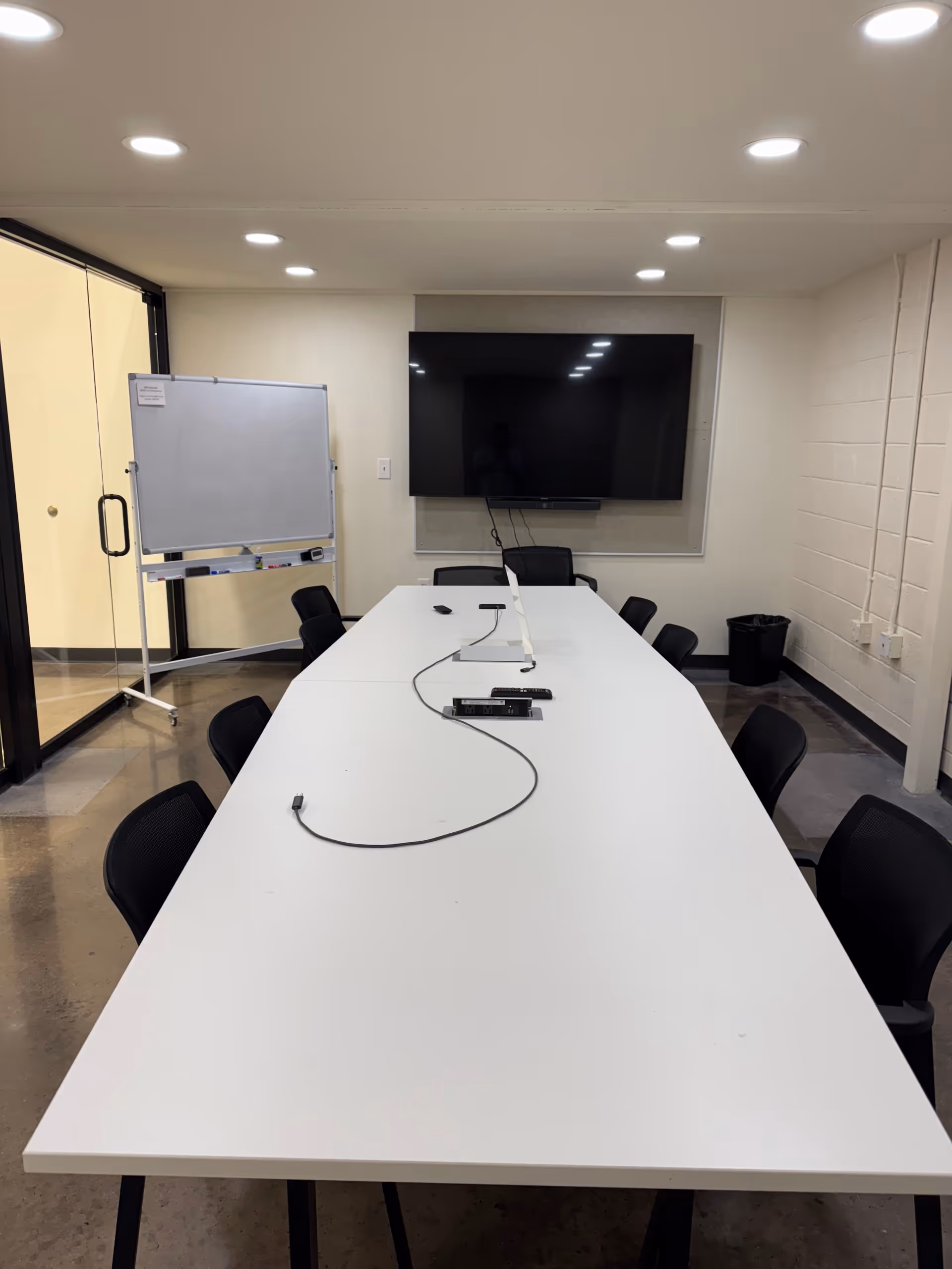 A long white conference table with chairs, whiteboard, and a wall-mounted TV.