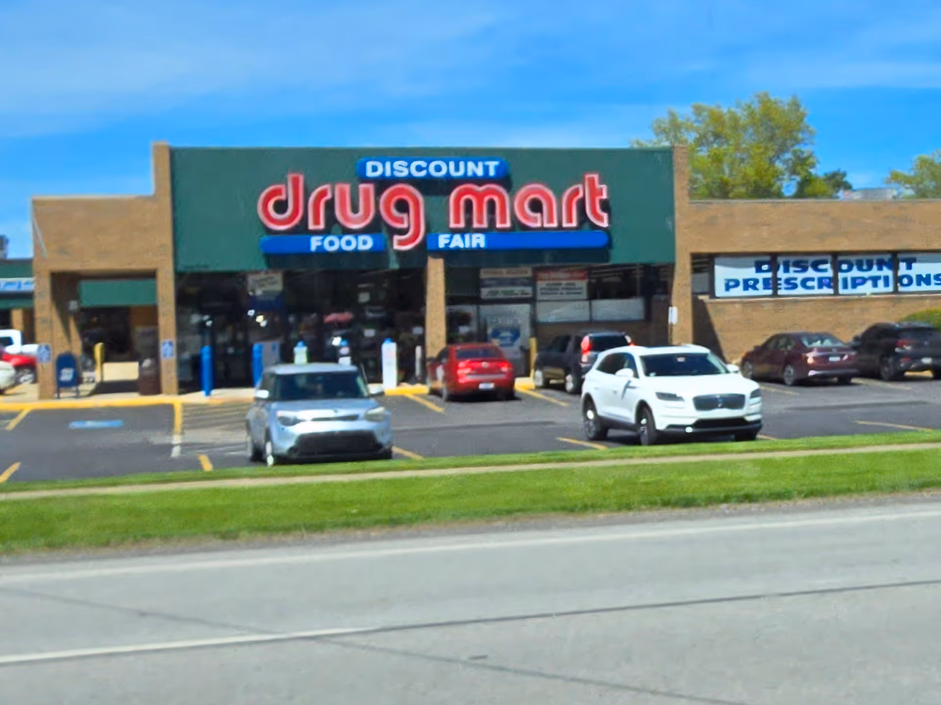 Exterior storefront of Discount Drug Mart with cars in a parking lot.