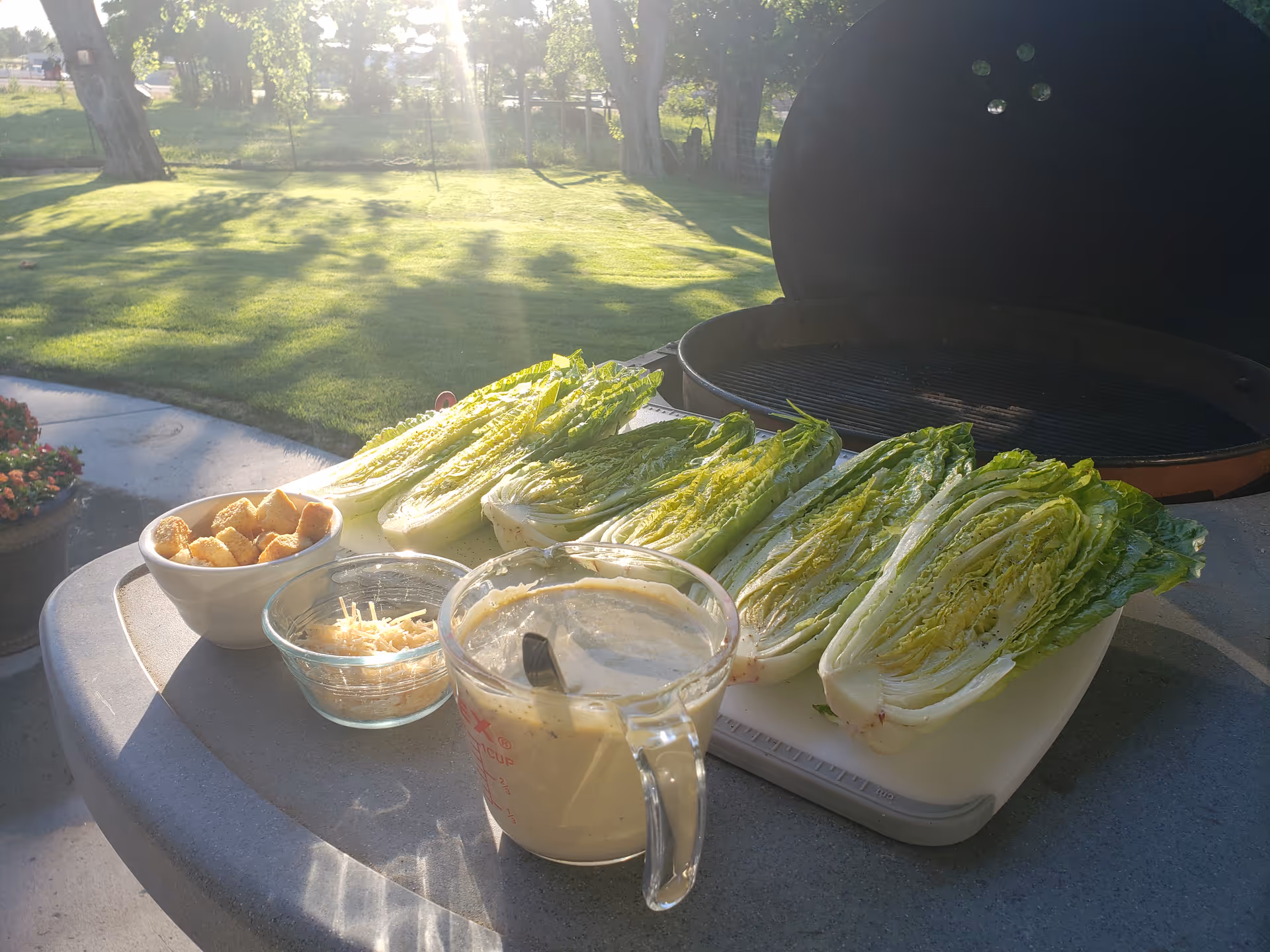 Outdoor grilling setup on a patio table with lettuce and condiments.