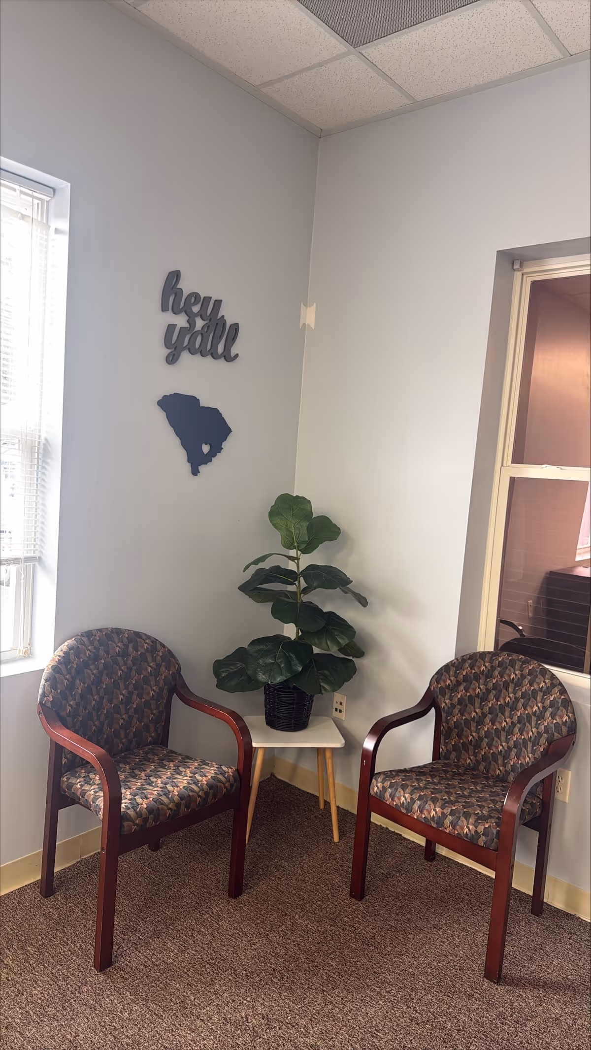 Two patterned chairs surround a small table with a potted plant in a bright waiting area.