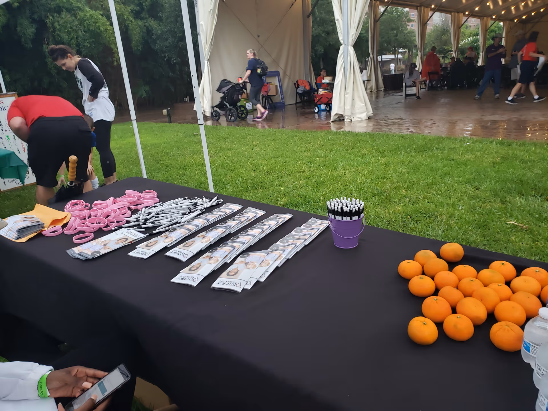Outdoor event booth with brochures, orange fruits, and pens on a black table.