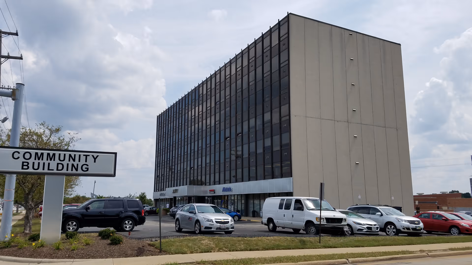 Tall beige multi-story building with glass windows, parking lot, and a 'Community Building' sign.