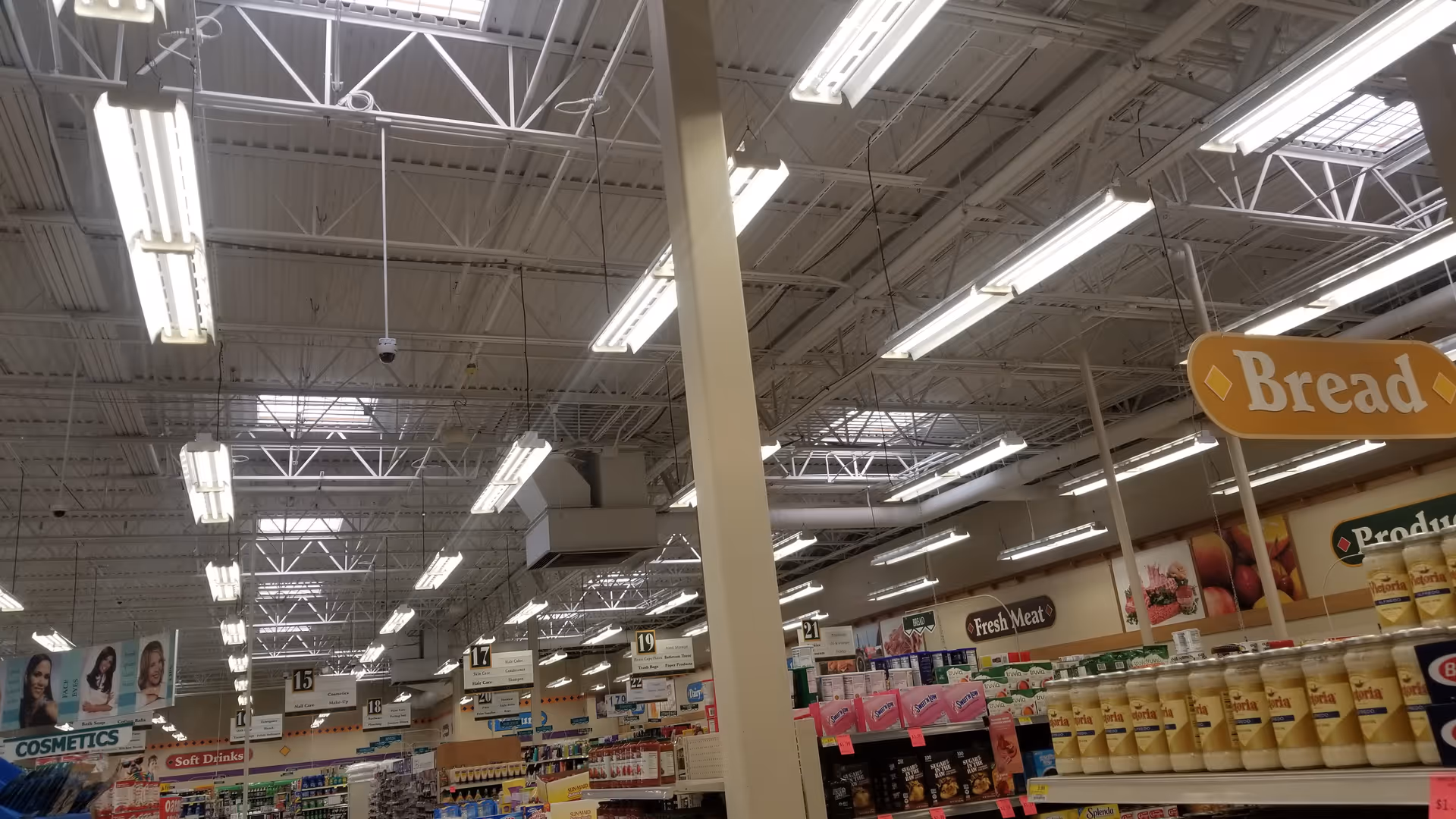 Bright grocery store interior with shelves, overhead lights, and a bread sign.