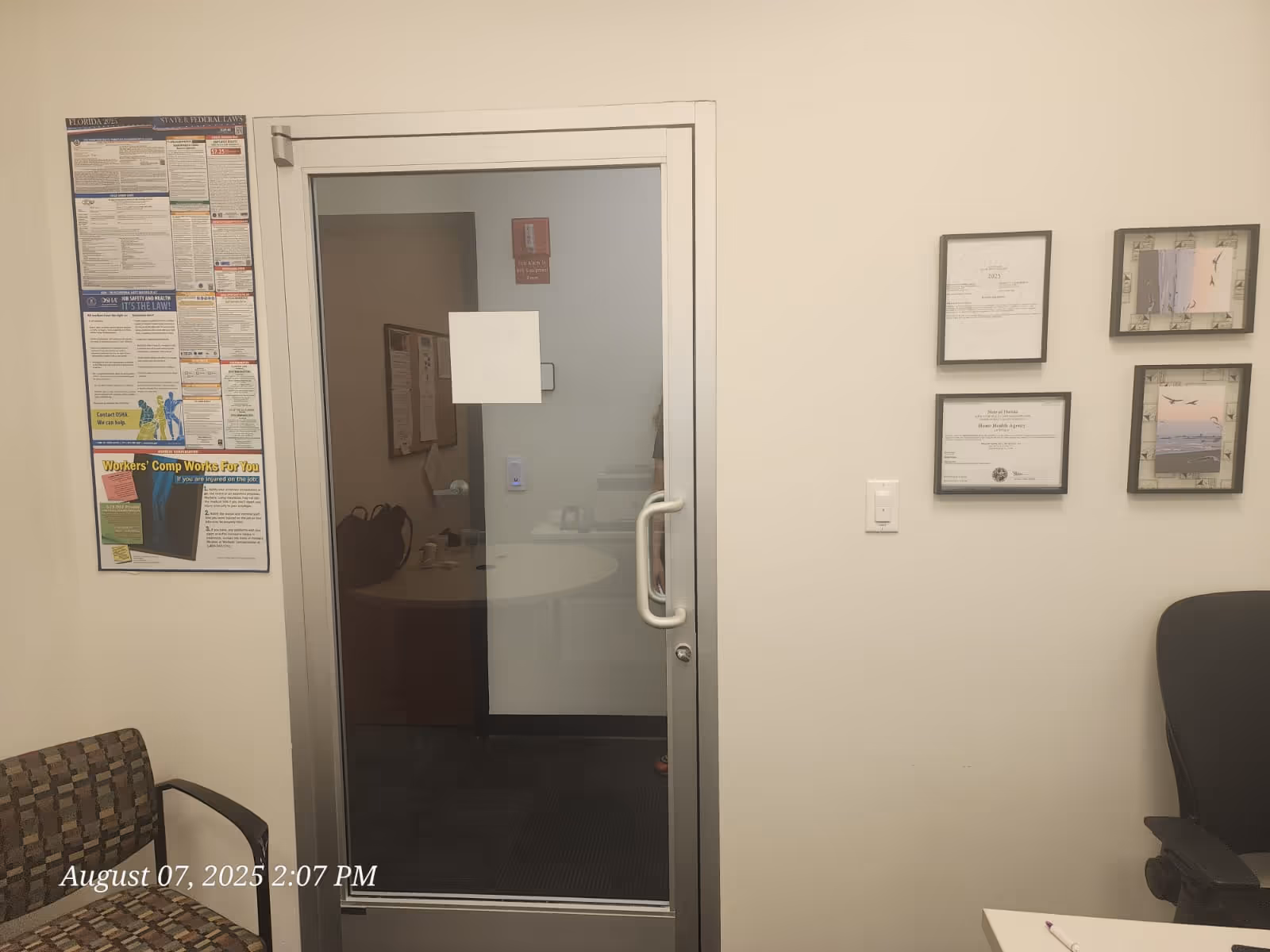 Interior office area with glass door, framed certificates, and a waiting chair.