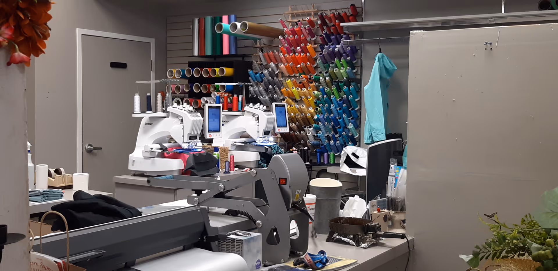 Indoor sewing workshop with two sewing machines, colorful threads, fabric bolts, and organized tools.