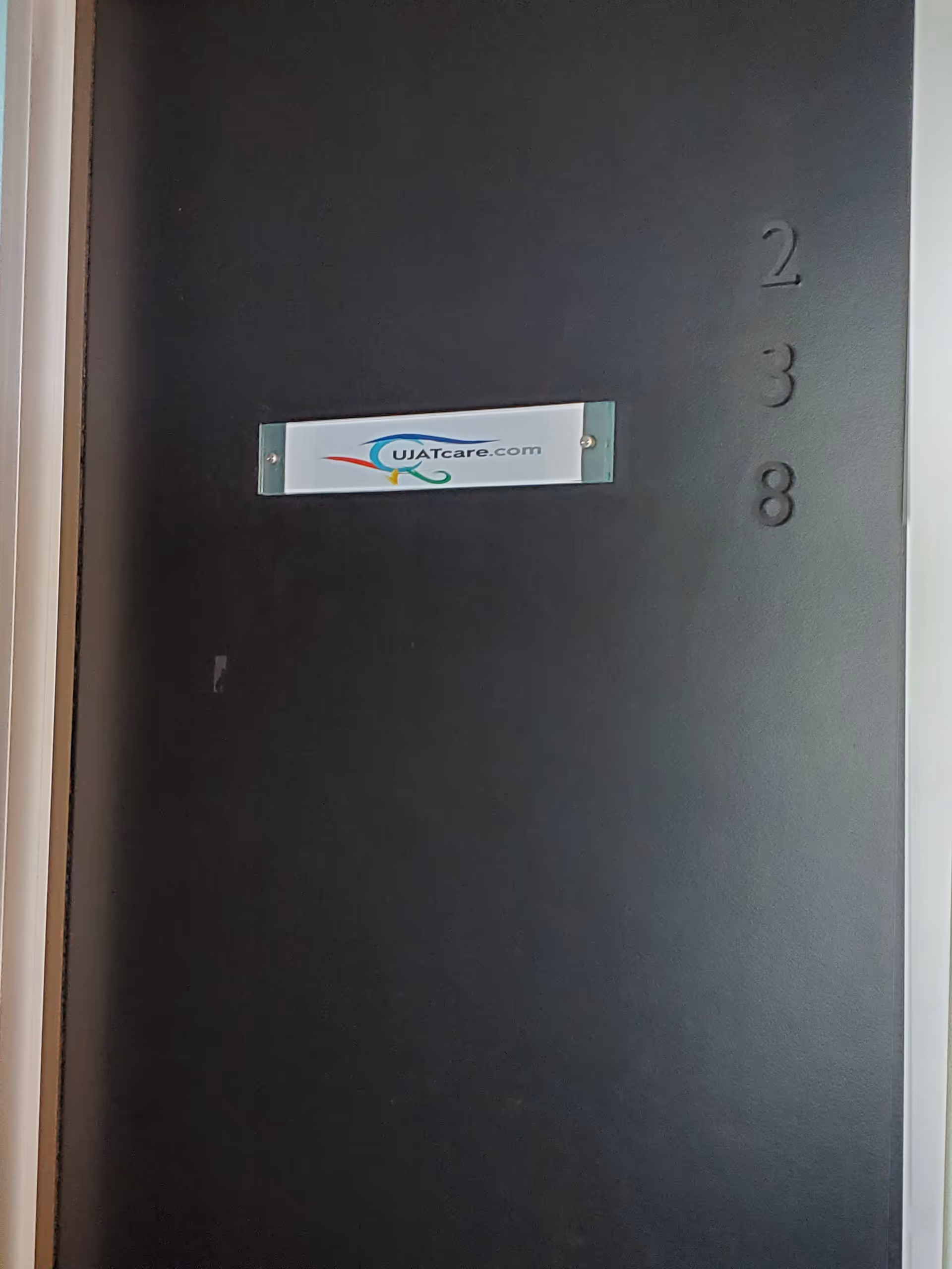 Dark interior door with a Ujatcare sticker and unit numbers 2, 3, 8.