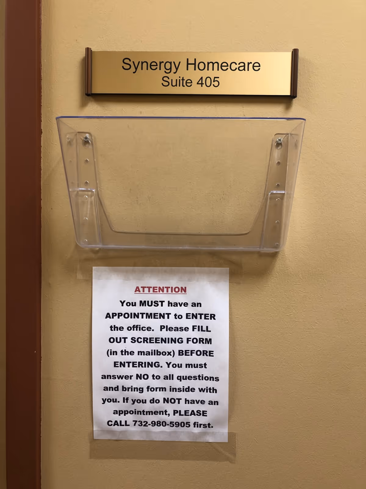 Interior wall with Synergy Homecare Suite 405 sign and screening notice.