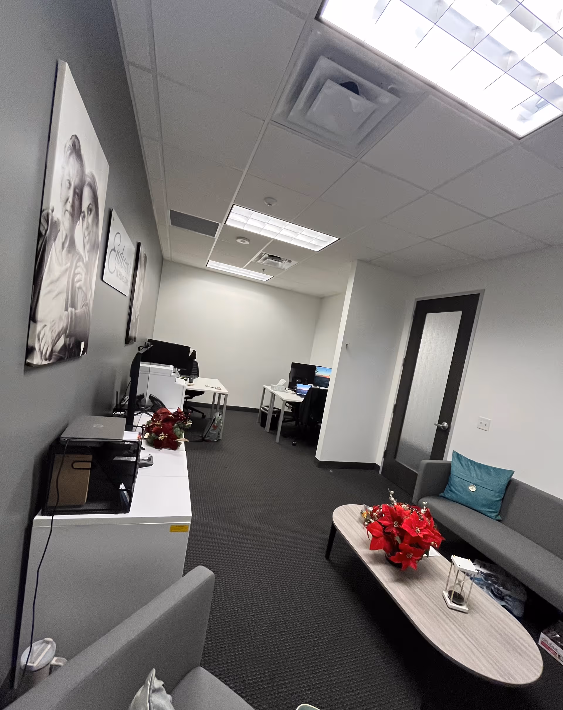 Small office and seating area inside a senior care facility, with computers and red flower arrangements.