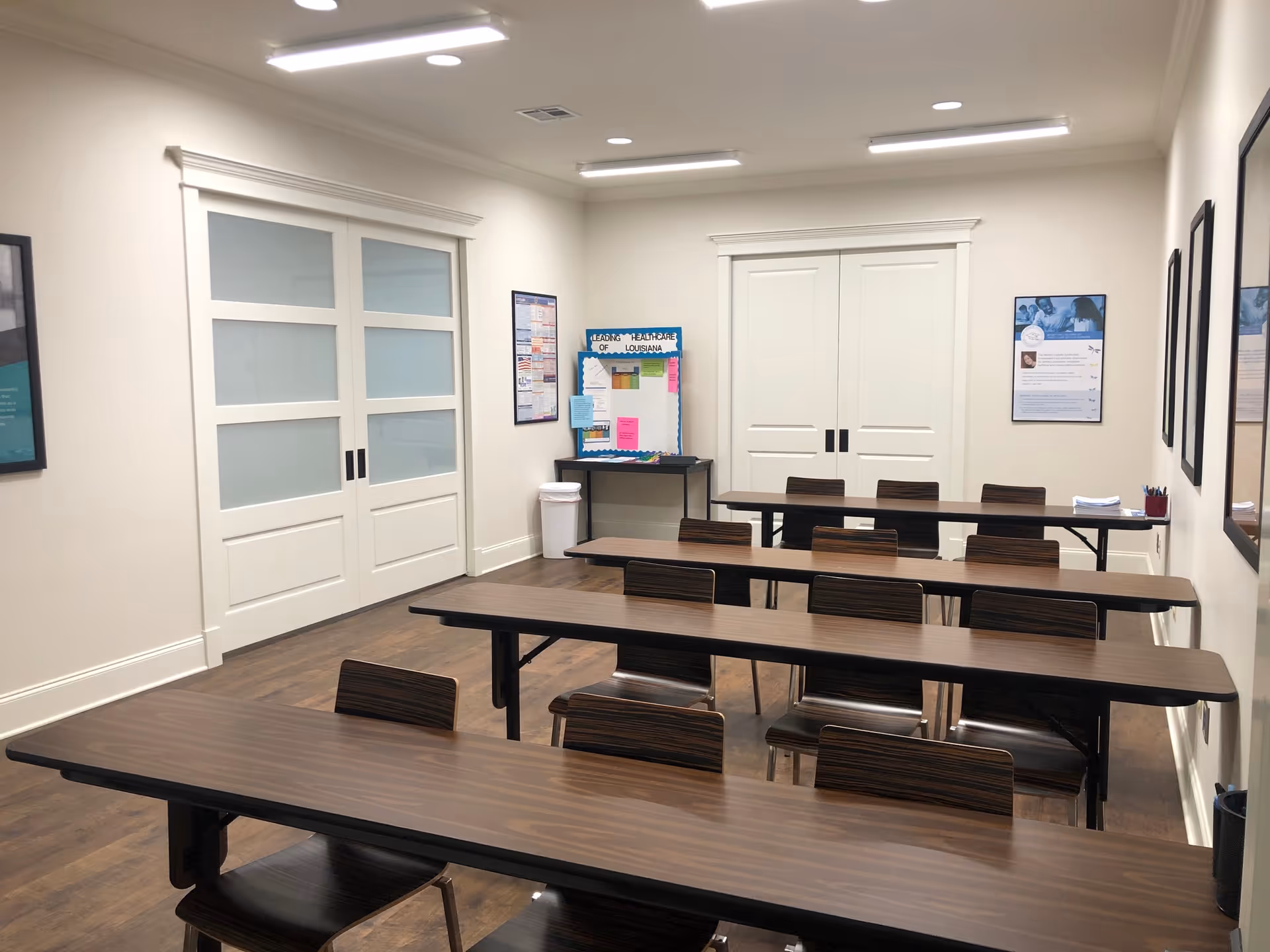 Empty classroom-style room with long brown desks, chairs, and wall posters.