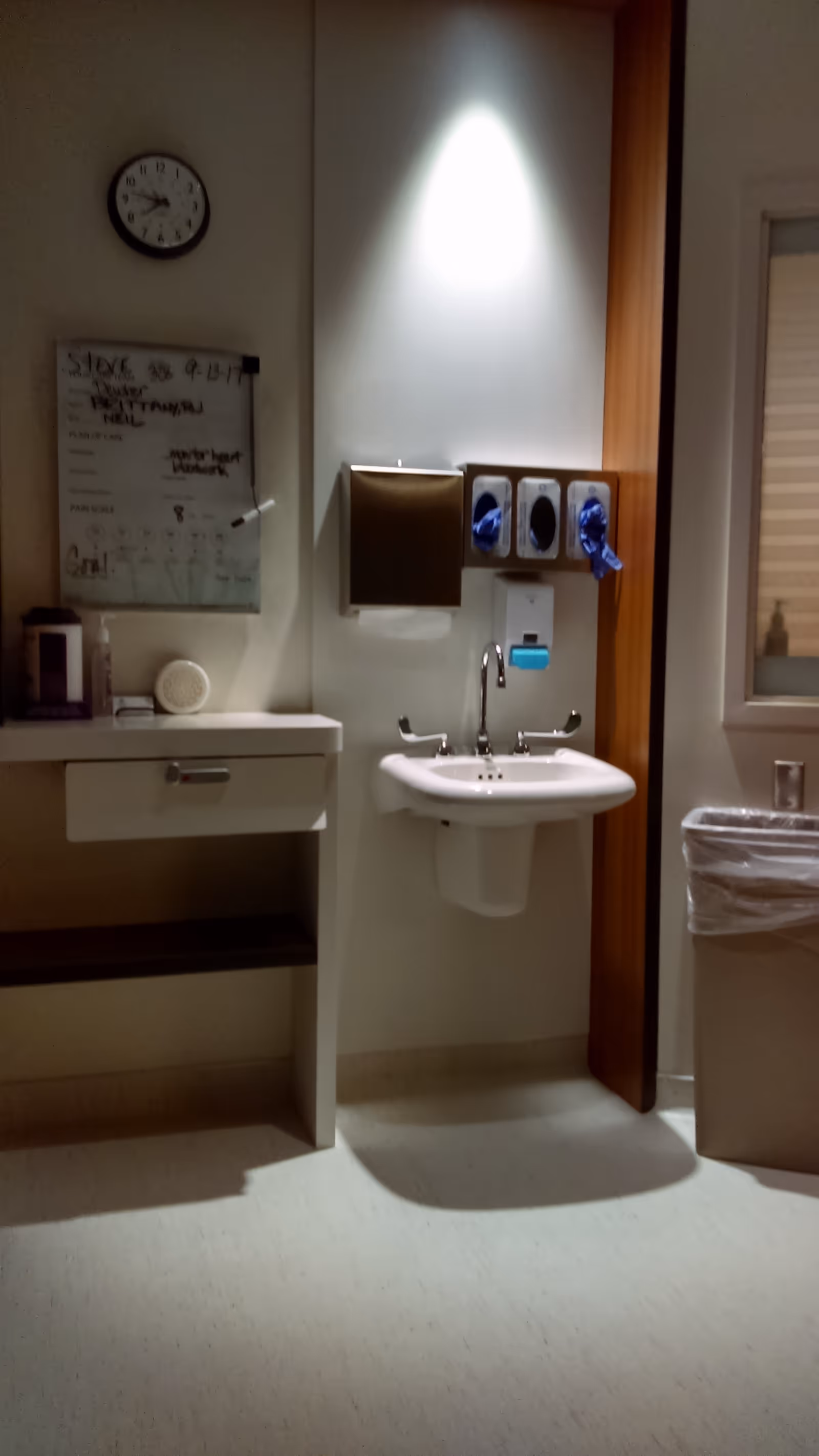 Bathroom sink area with faucet, soap dispensers, paper towel dispenser, clock, and cabinet.