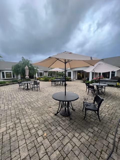 Outdoor brick courtyard with tables, chairs, and umbrellas in front of a facility.