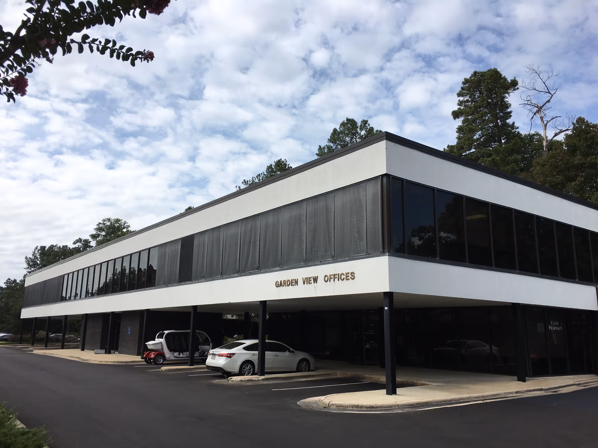 Two-story modern office building with glass windows and parked cars in front.