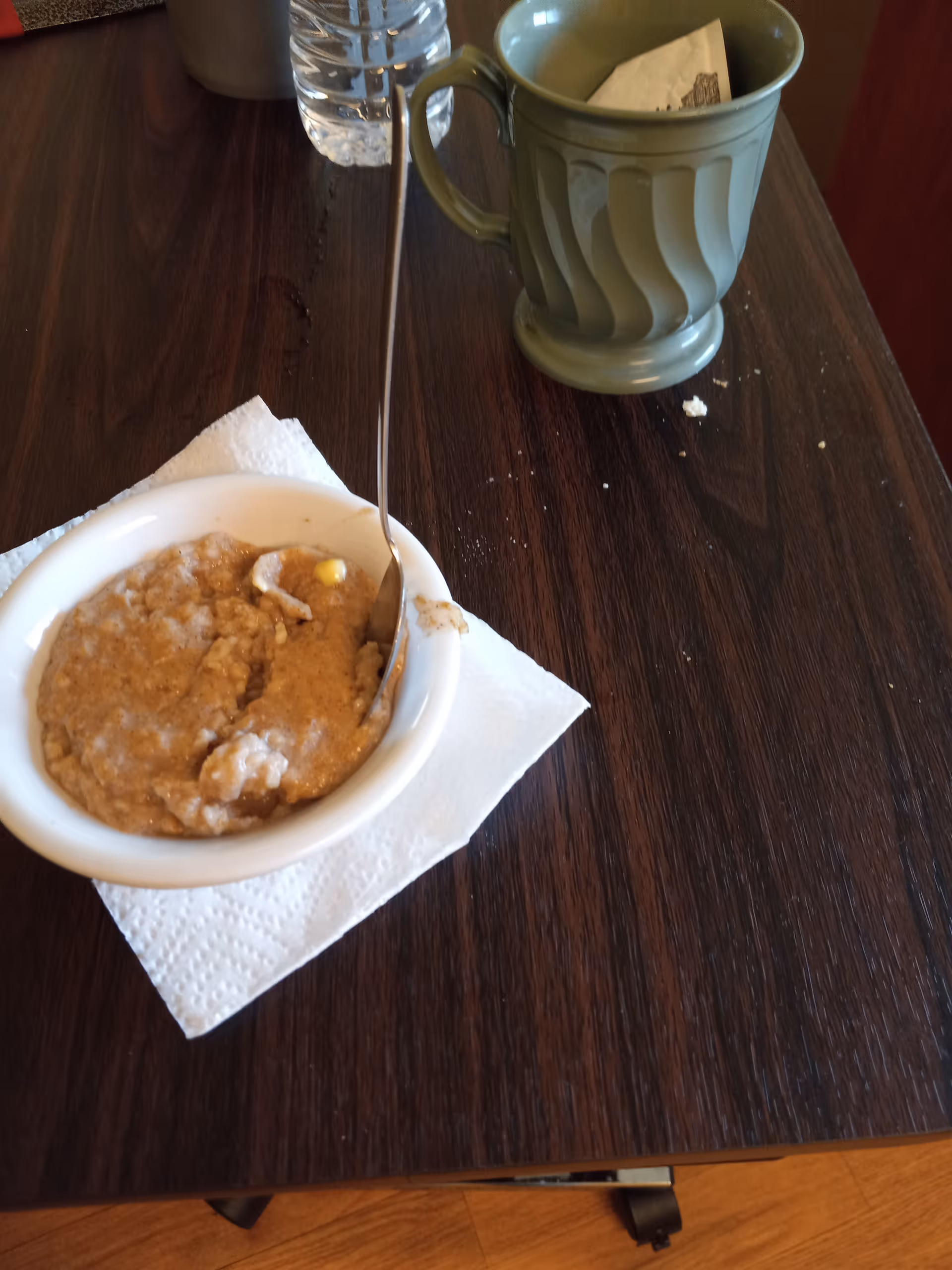 Bowl of oatmeal-like dessert on dark wood table beside a green mug.