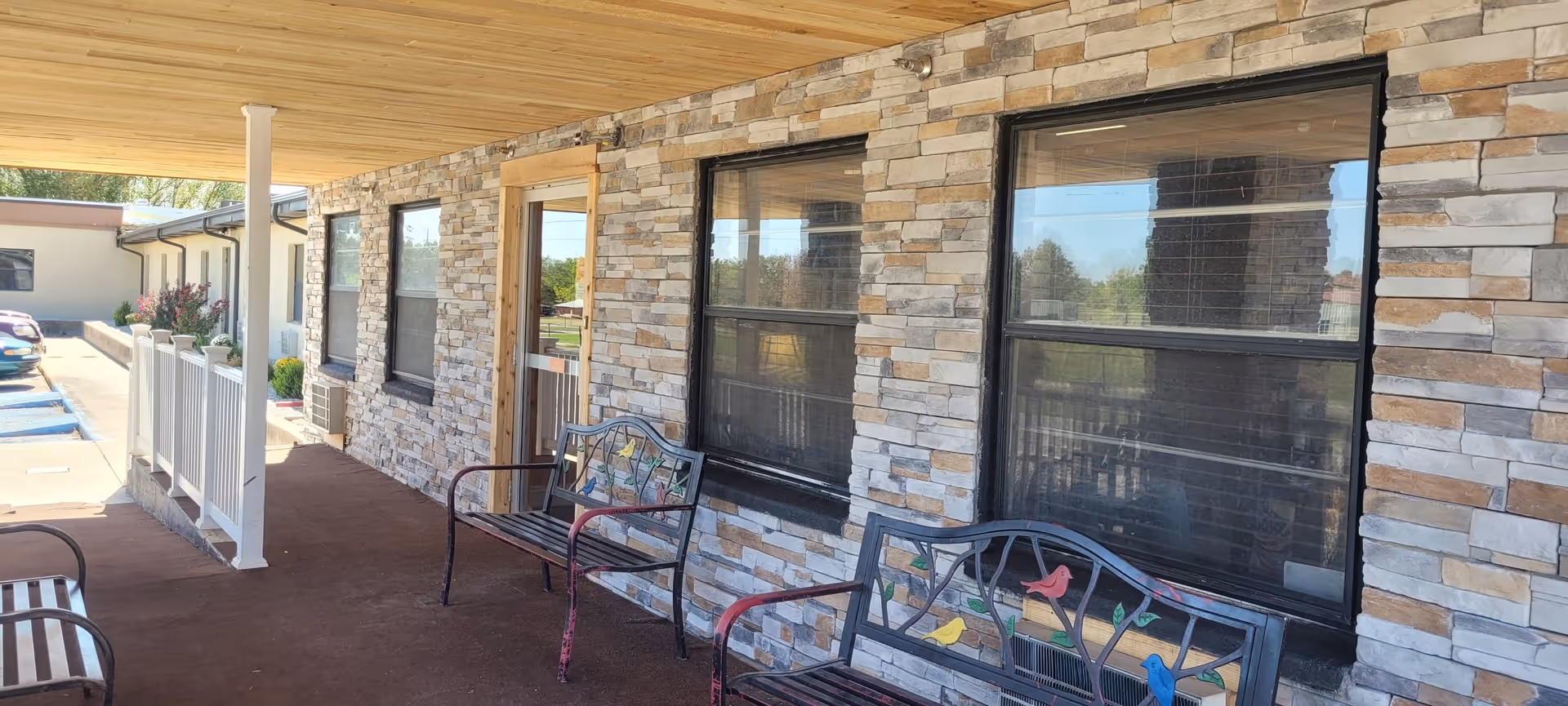 Stone-clad building exterior with a covered walkway and metal benches on the porch.