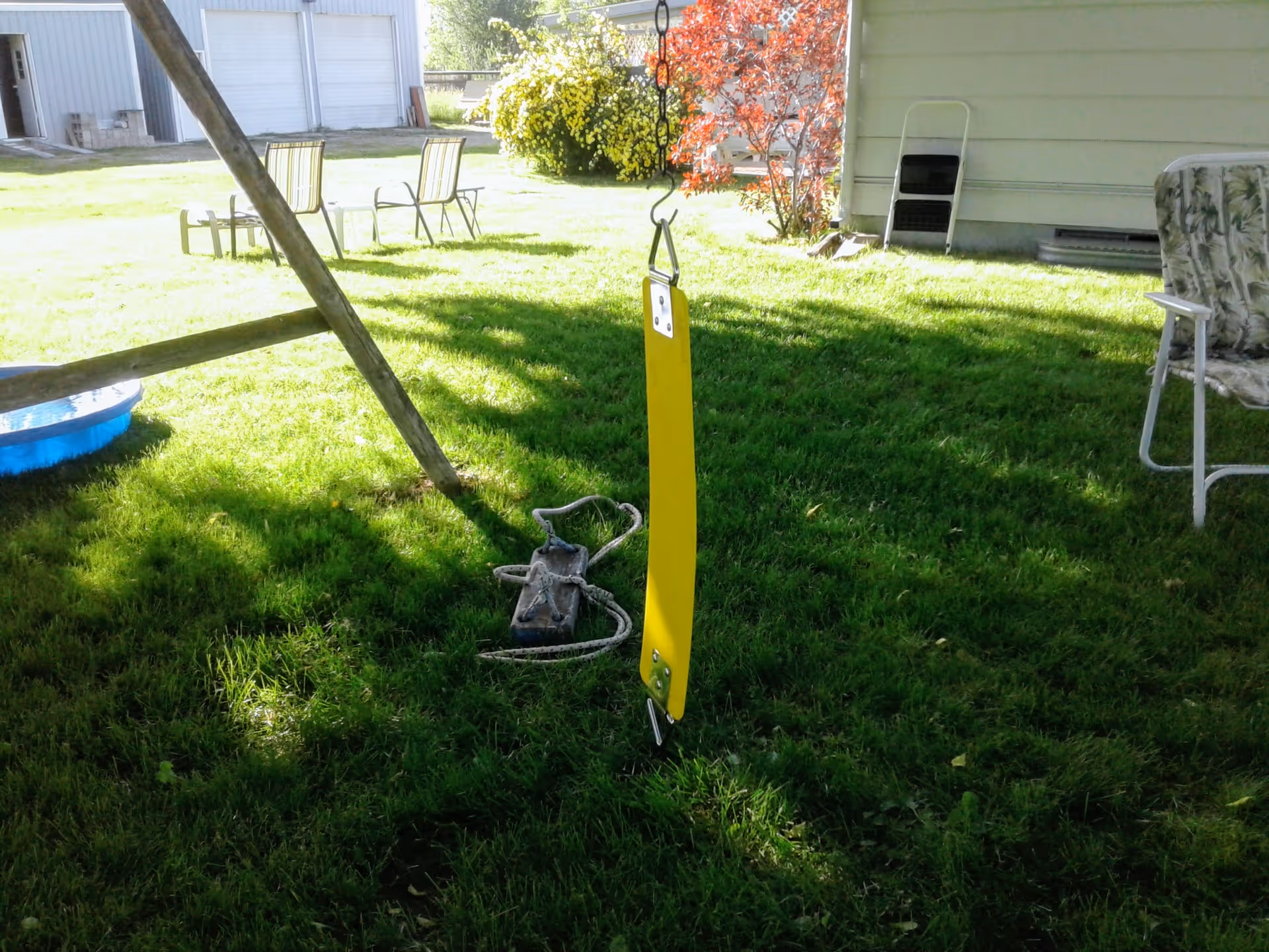 Grassy backyard with a yellow swing post, chairs, and a blue plastic pool.