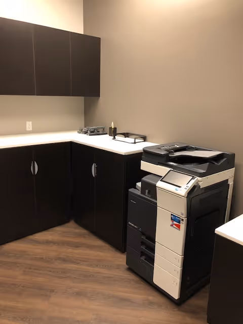 Utility kitchenette with dark cabinets, white countertops, and a multifunction printer.