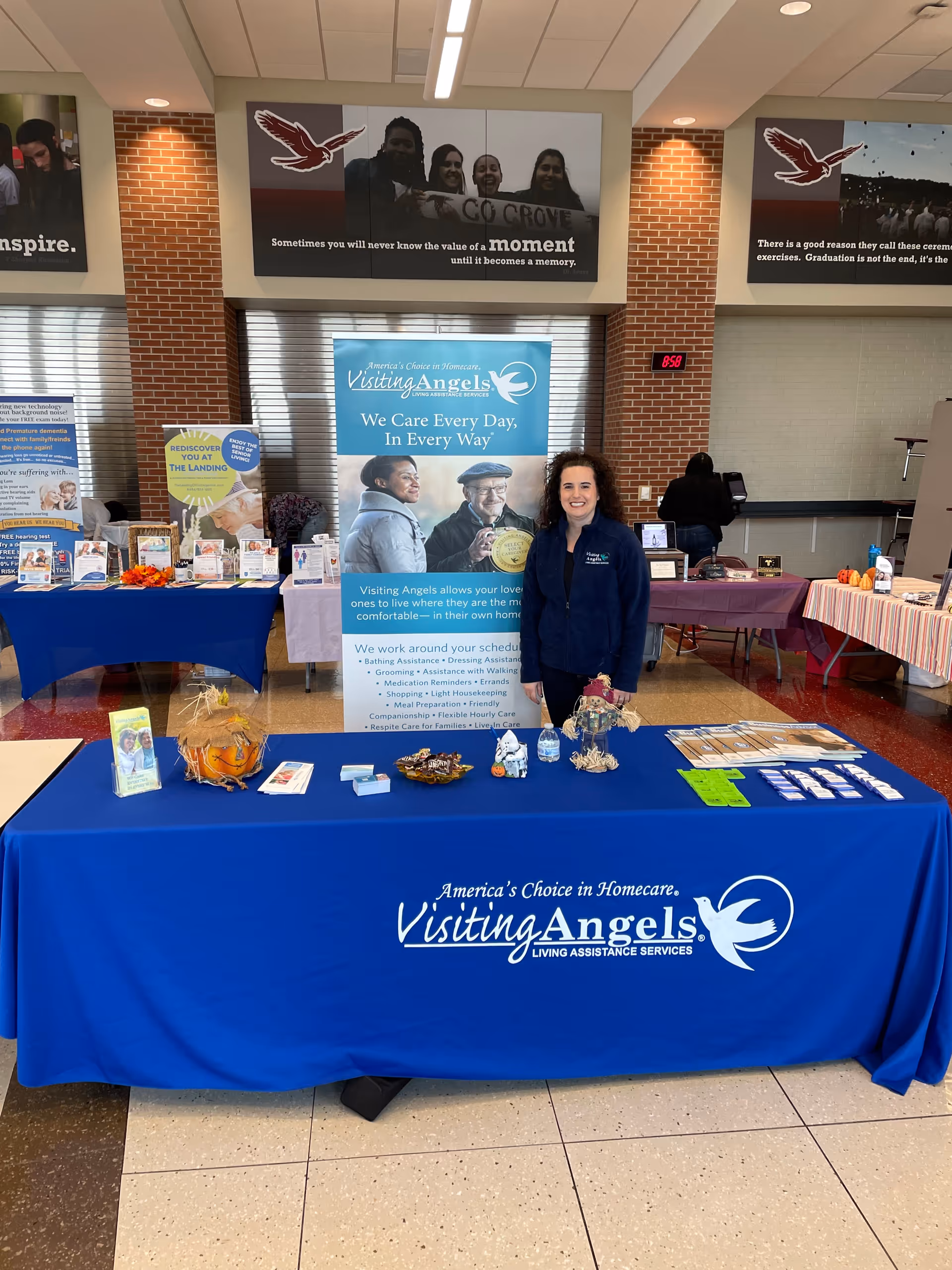 Smiling staff member at a Visiting Angels information booth inside an indoor facility.
