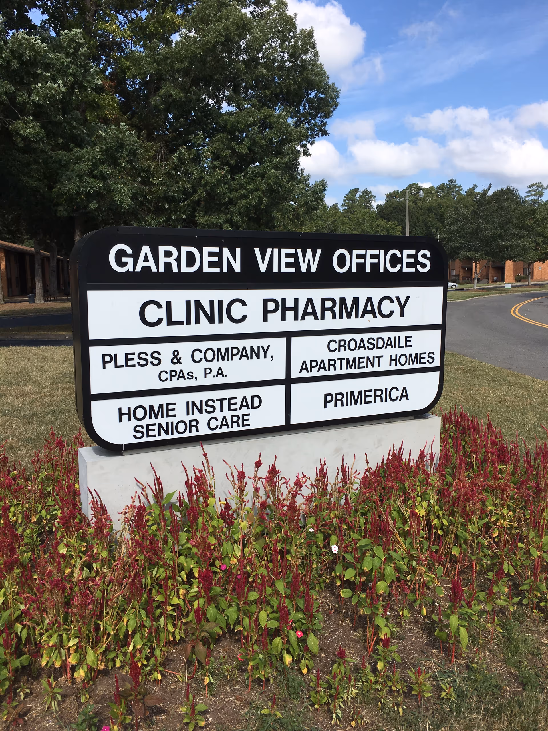 A large sign reading Garden View Offices and Clinic Pharmacy sits near flowering shrubs outdoors.