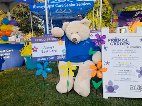A large teddy bear mascot under a blue canopy at an outdoor fundraiser event.