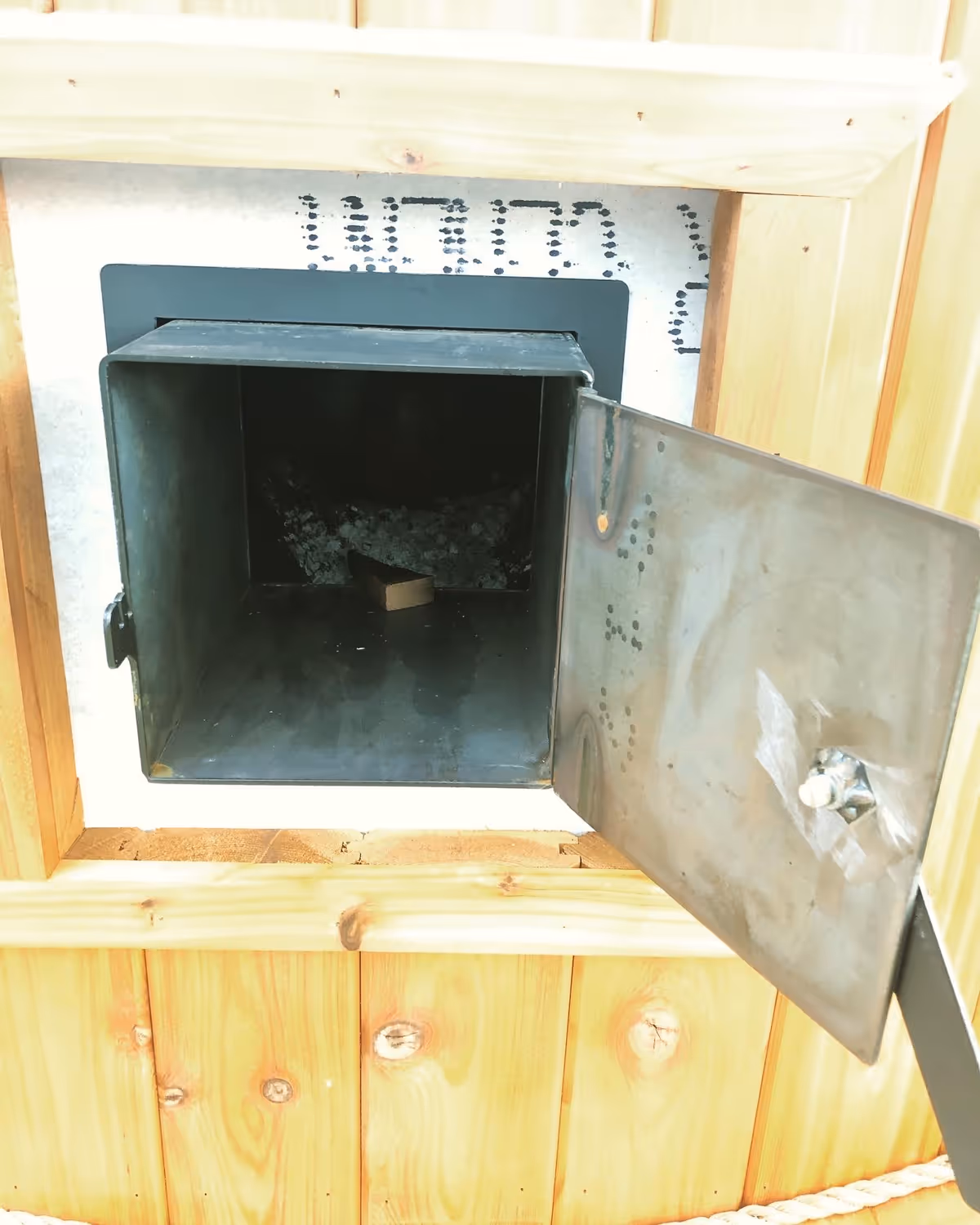 Open metal hatch in a wooden wall reveals a dark interior with a small object.