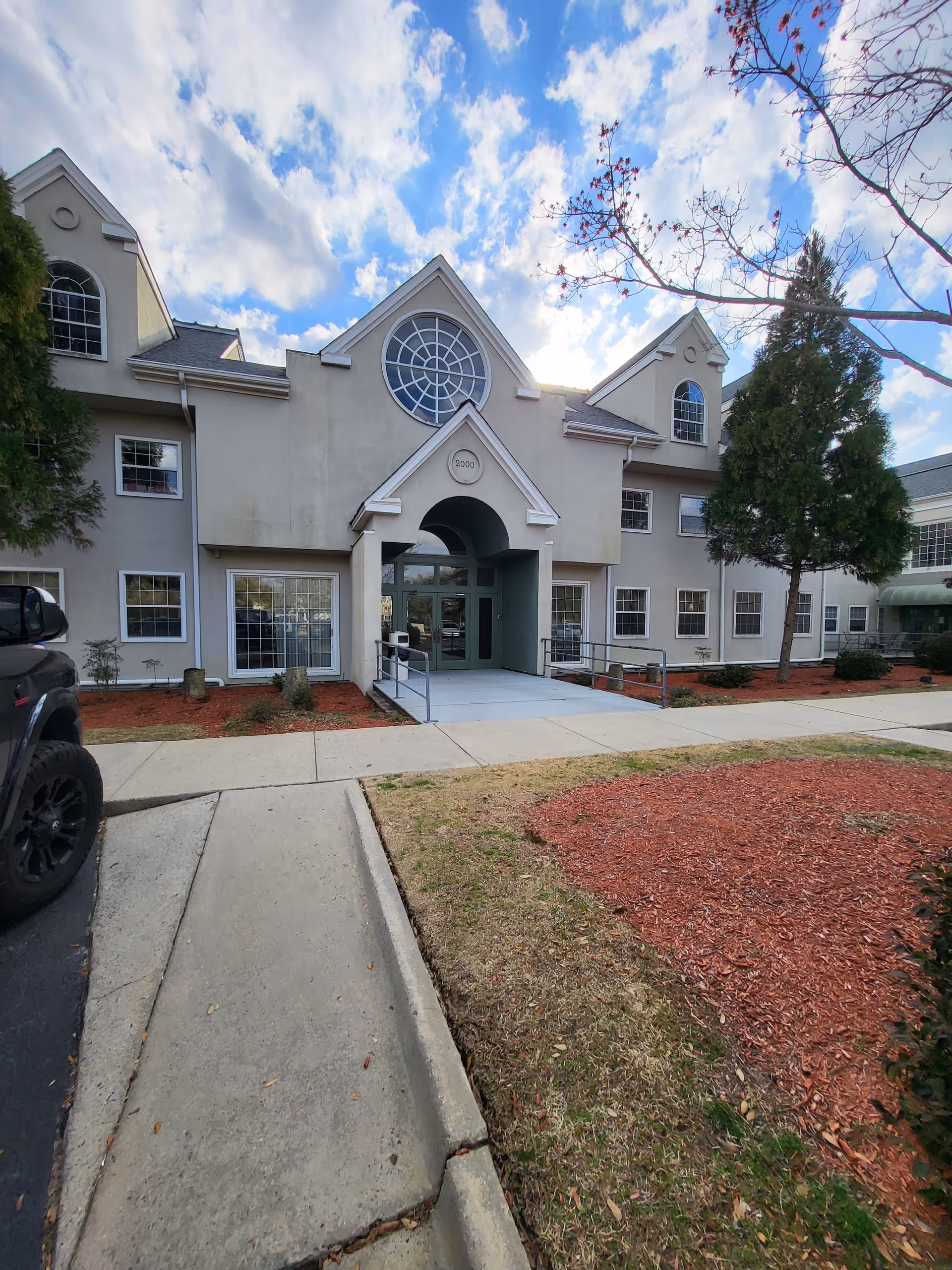 Front view of a senior living facility with arched entrance and manicured landscaping.
