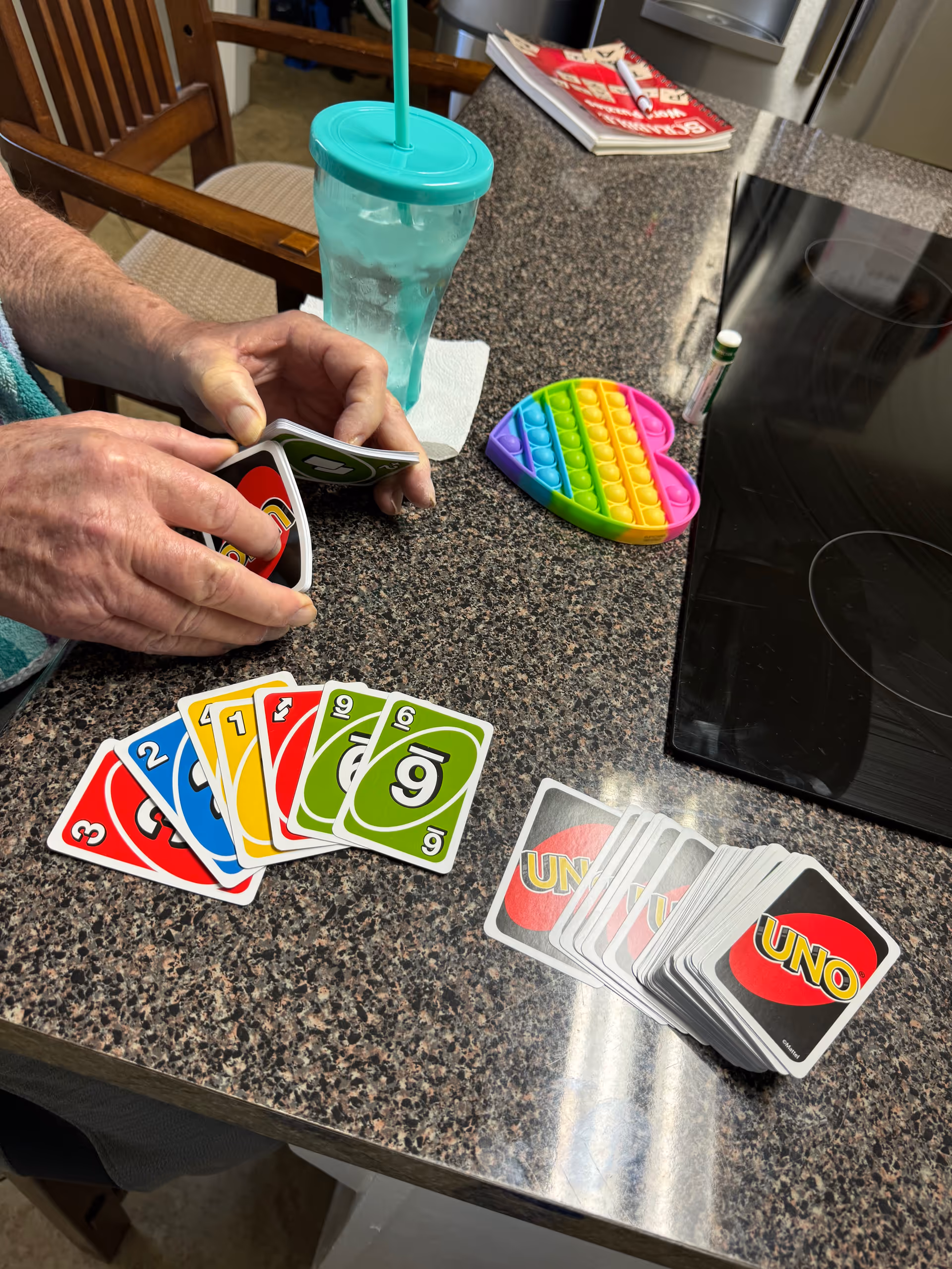 A person's hands hold UNO cards on a kitchen counter beside a turquoise tumbler.