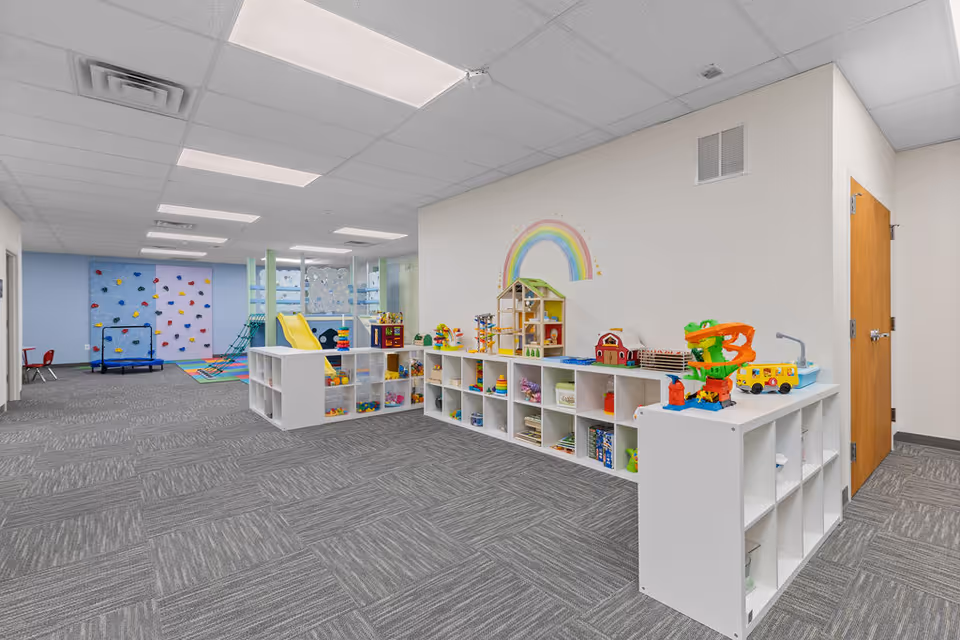 Bright indoor children's play area with shelving, toys, and a rainbow mural.